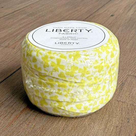 A roll of yellow and white fabric with a label that says "LIBERTY FABRIC" on a wooden surface.
