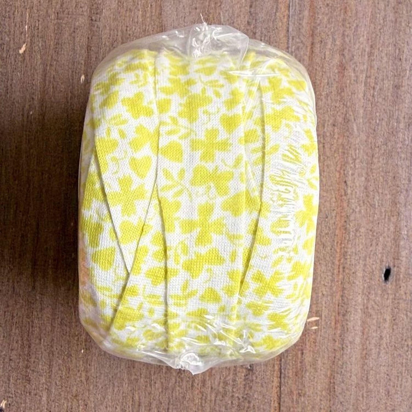 A roll of yellow and white fabric with a floral pattern is wrapped in plastic and placed on a wooden surface.