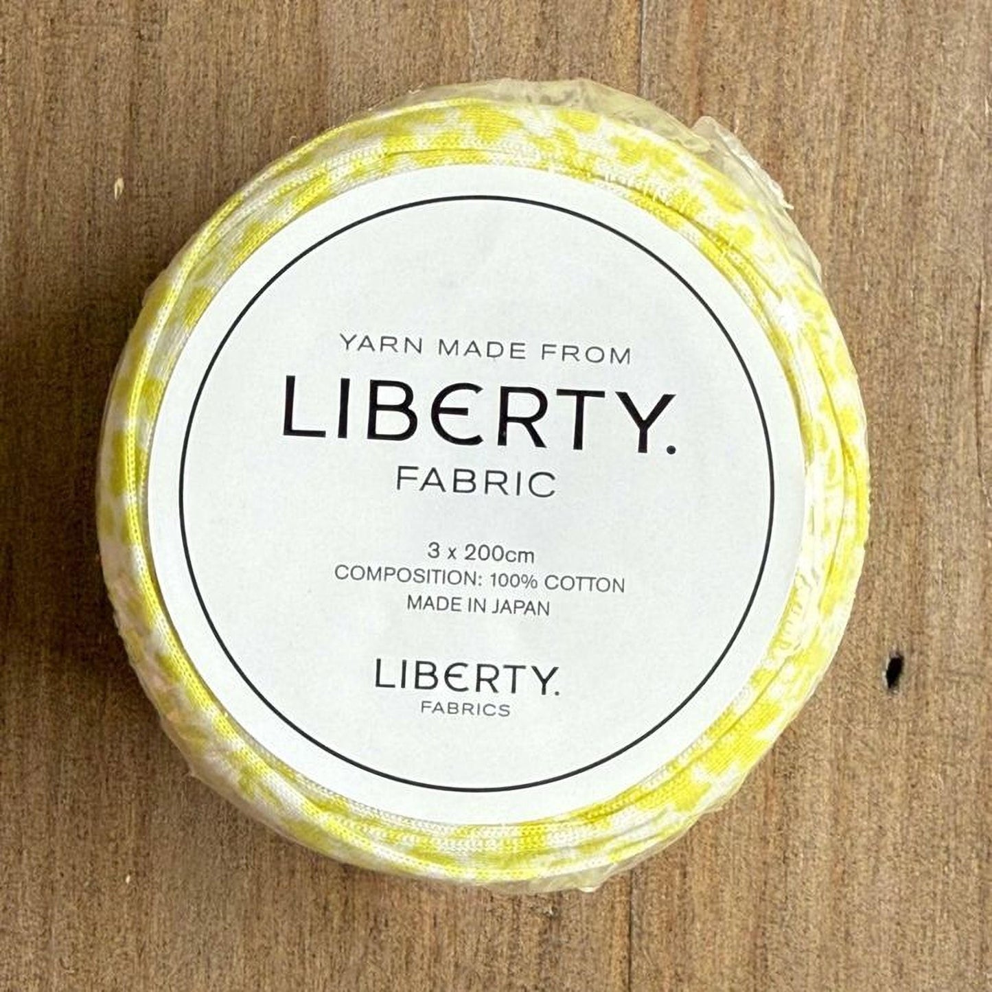 A white label with black text on a yellow fabric roll, indicating that the yarn is made from Liberty fabric.