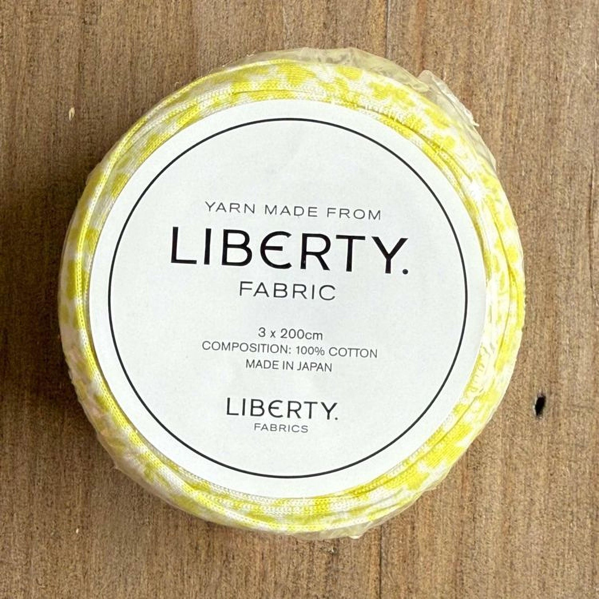 A white label with black text on a yellow fabric roll, indicating that the yarn is made from Liberty fabric.