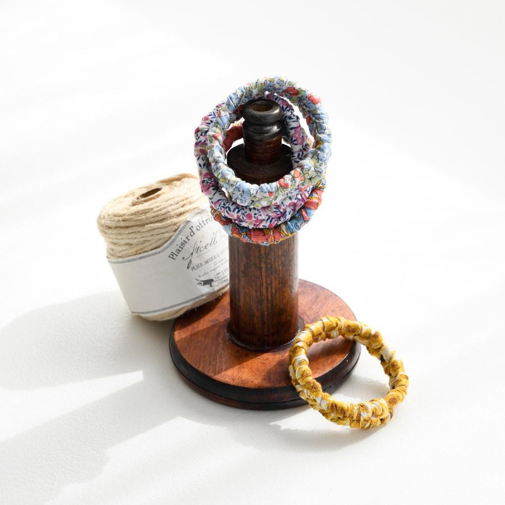 A wooden stand displaying a collection of colorful bracelets, a spool of thread, and a wooden spool of thread.