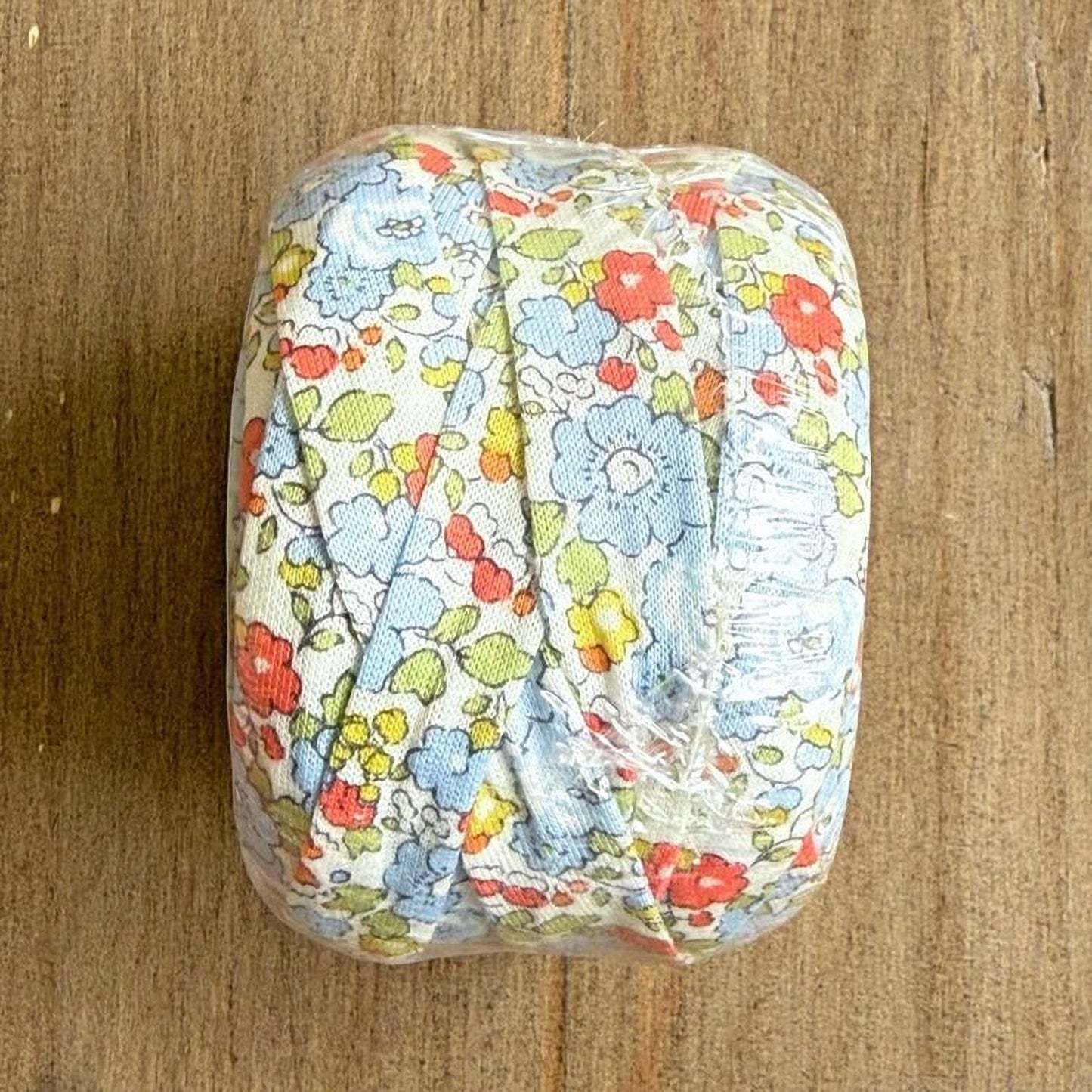 A roll of fabric with a floral pattern is placed on a wooden surface.