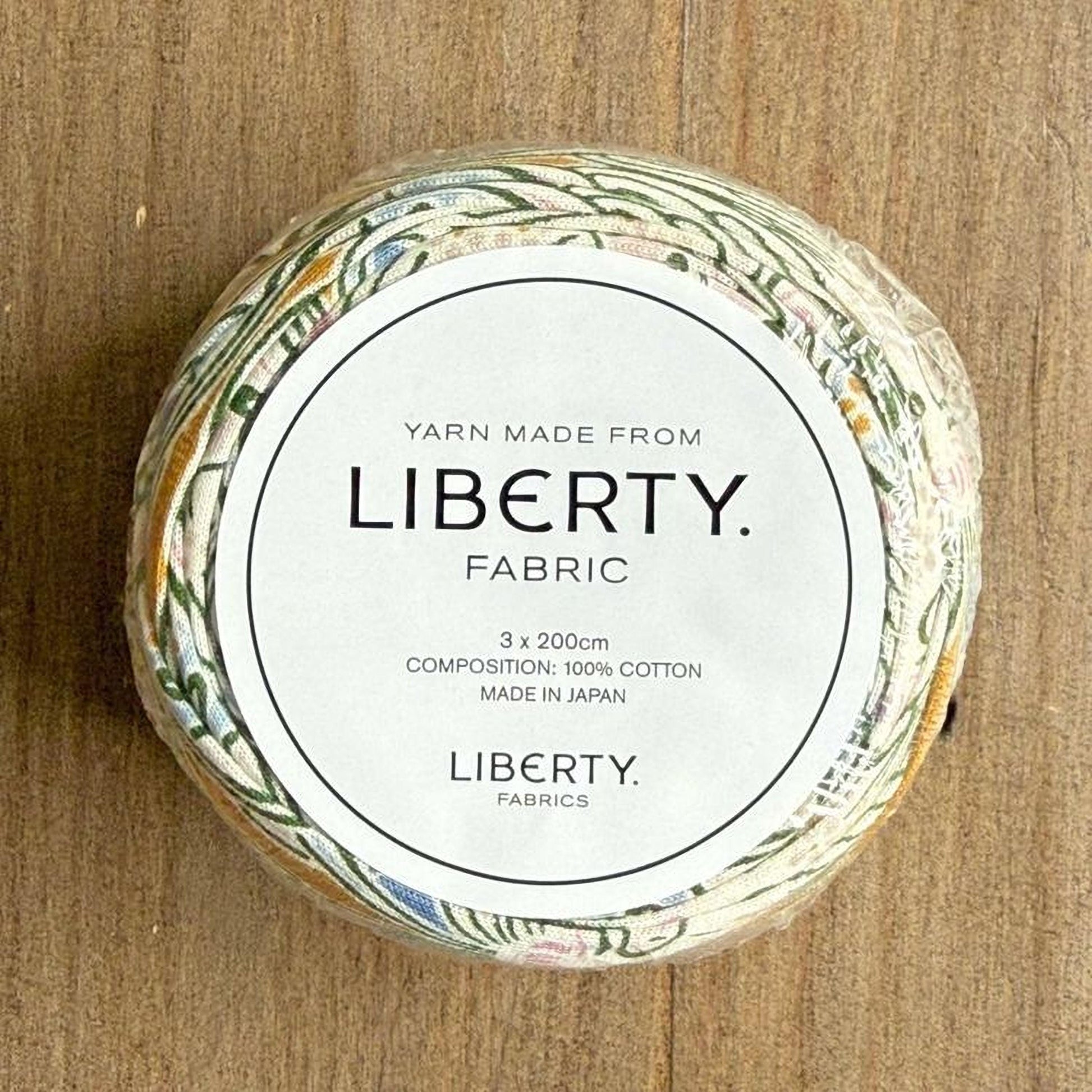 A spool of yarn made from Liberty fabric, with a label indicating it is composed of 100% cotton and is made in Japan.