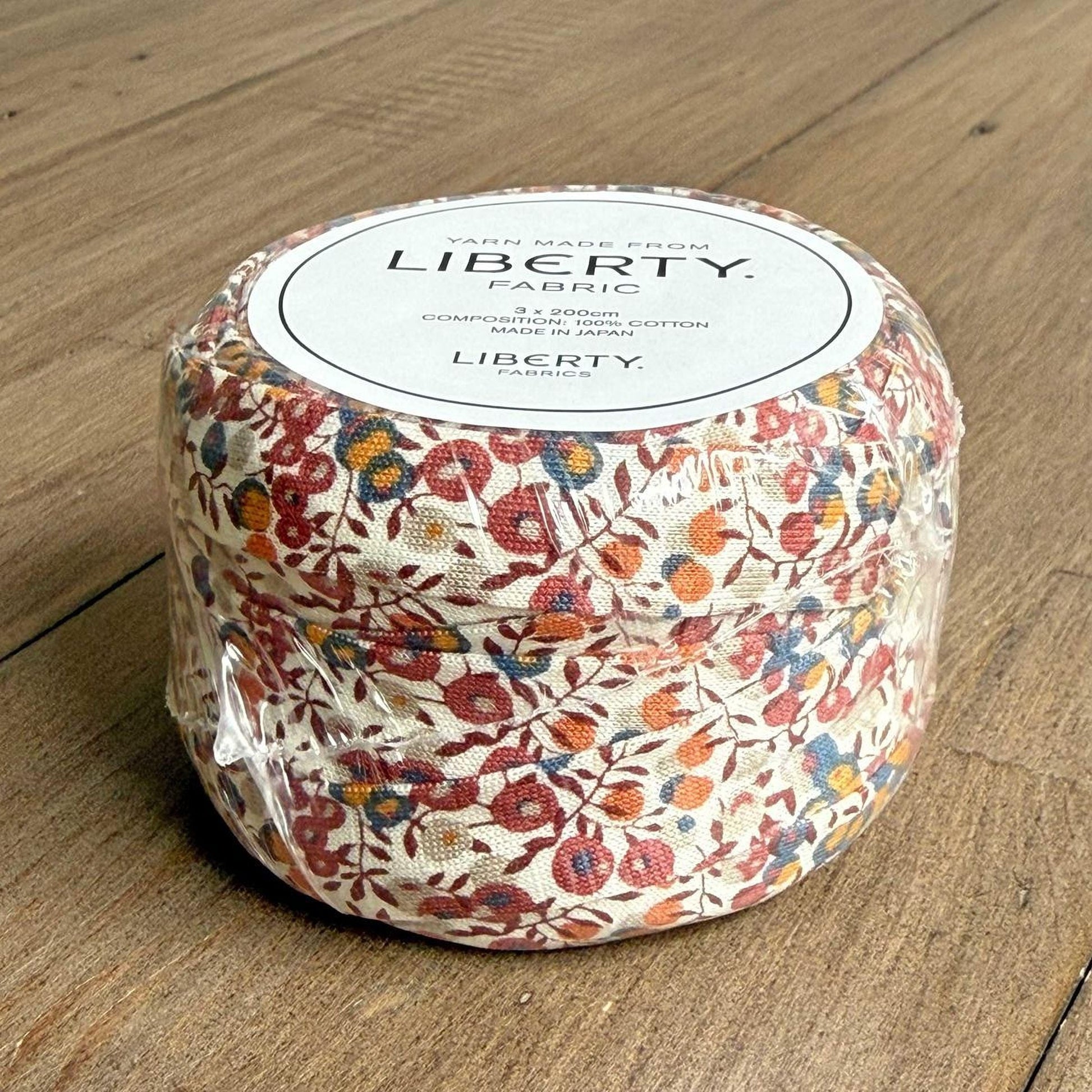 A package of Liberty Yarn Fabric, featuring a floral print design, is sitting on a wooden surface.