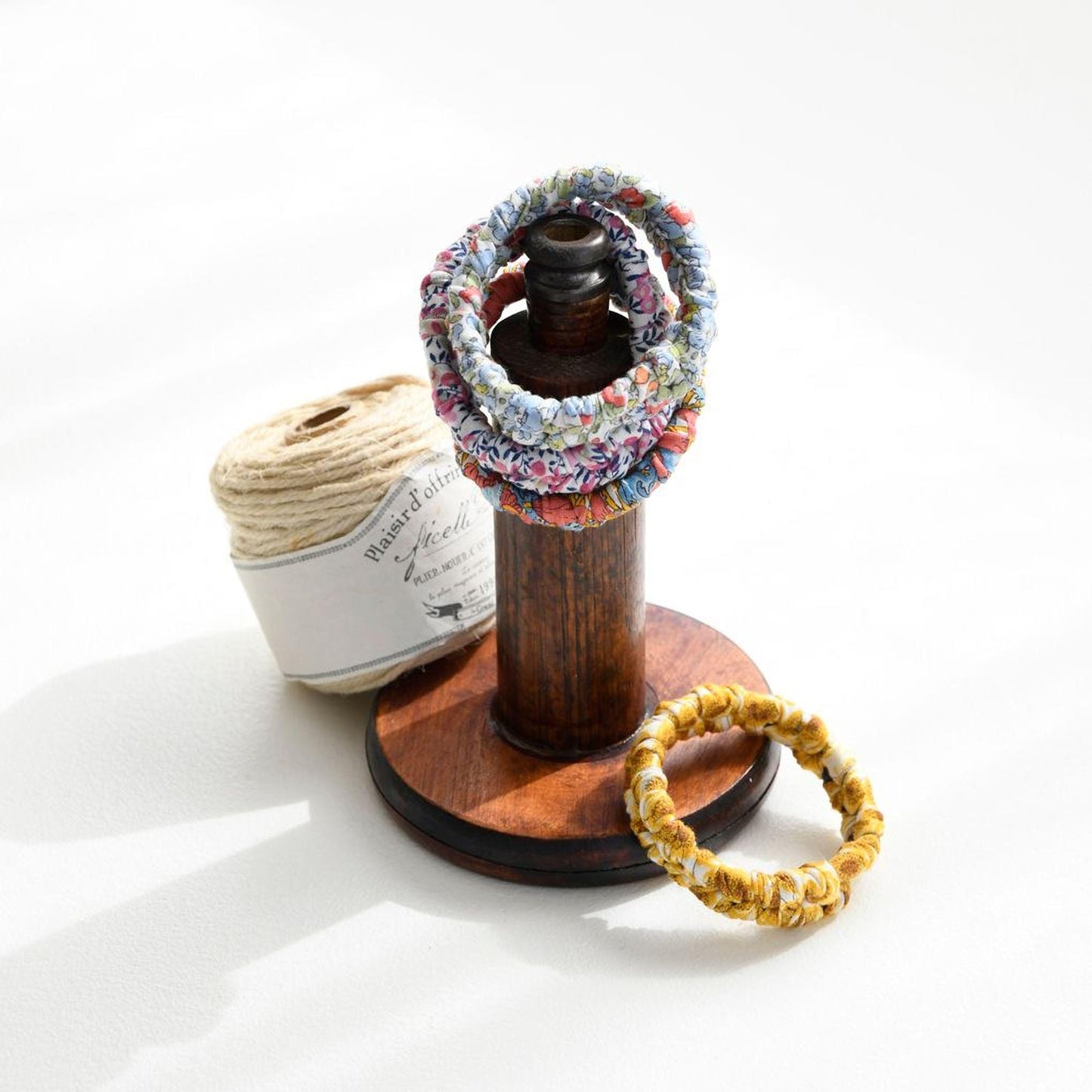 A wooden stand displaying a collection of colorful bracelets, a spool of thread, and a wooden spool of thread.