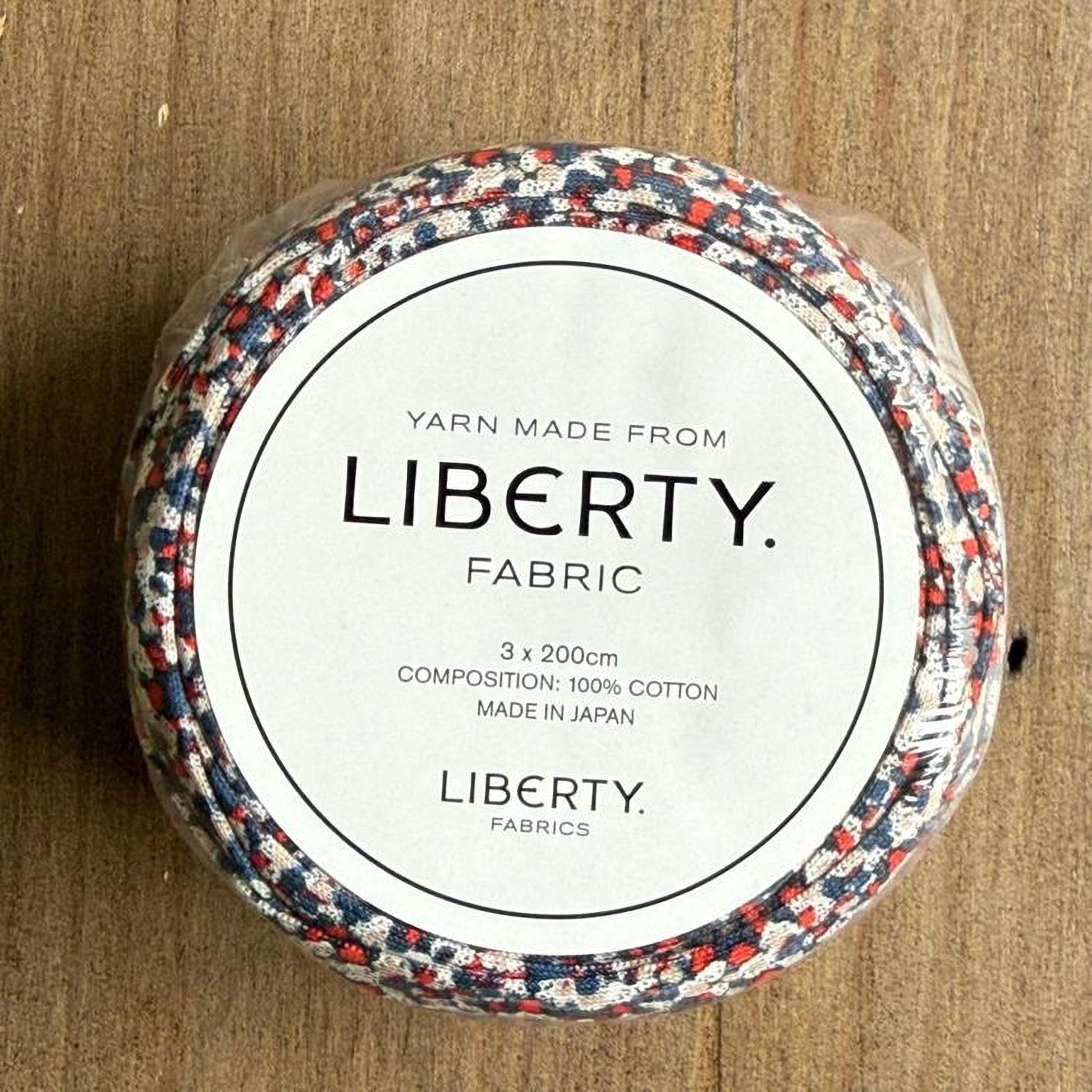 A package of Liberty fabric, made from 100% cotton, is shown on a wooden surface.