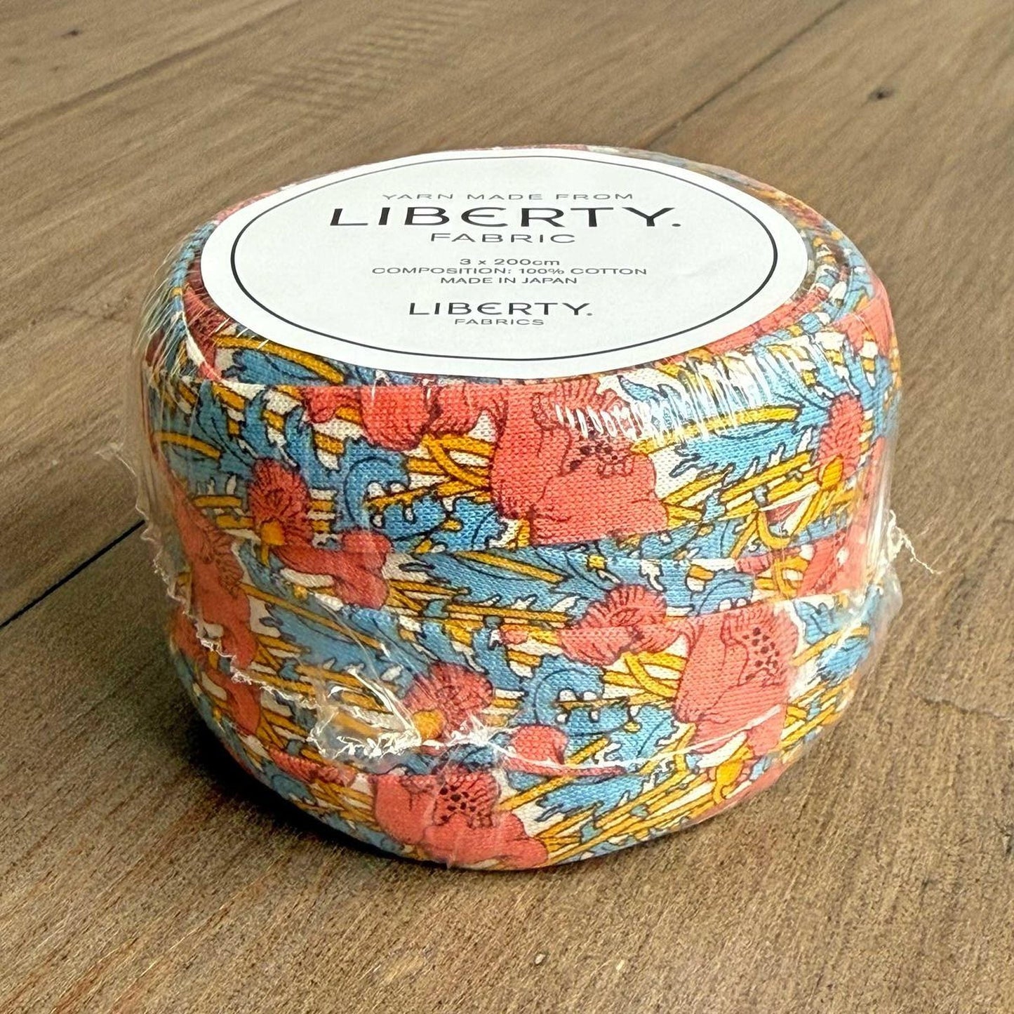 A container of fabric with a colorful floral pattern, sitting on a wooden surface.
