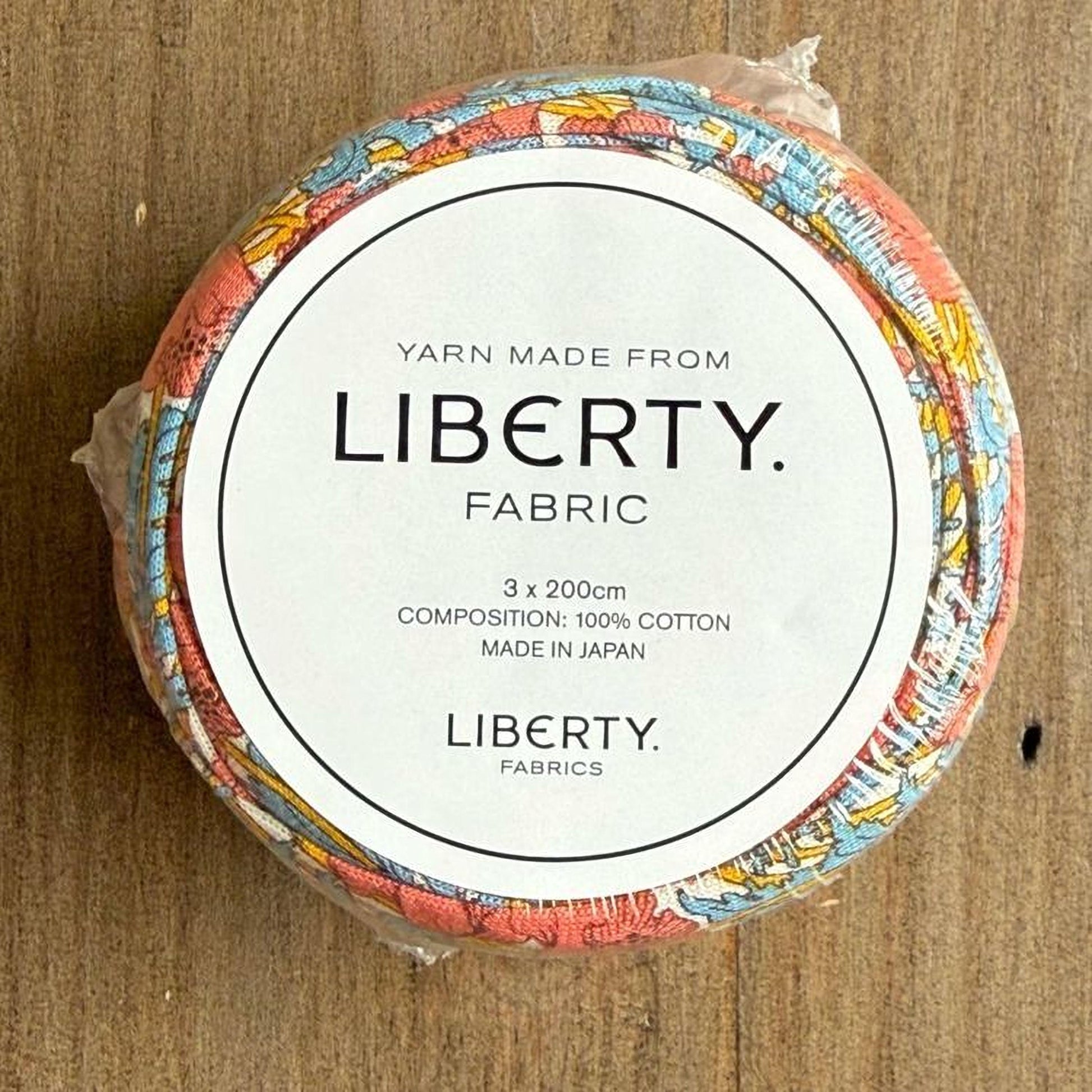 A circular object with a label that reads "Yarn Made from LIBERTY. Fabric" and "3 x 200cm COMPOSITION: 100% COTTON MADE IN JAPAN LIBERTY FABRICS".