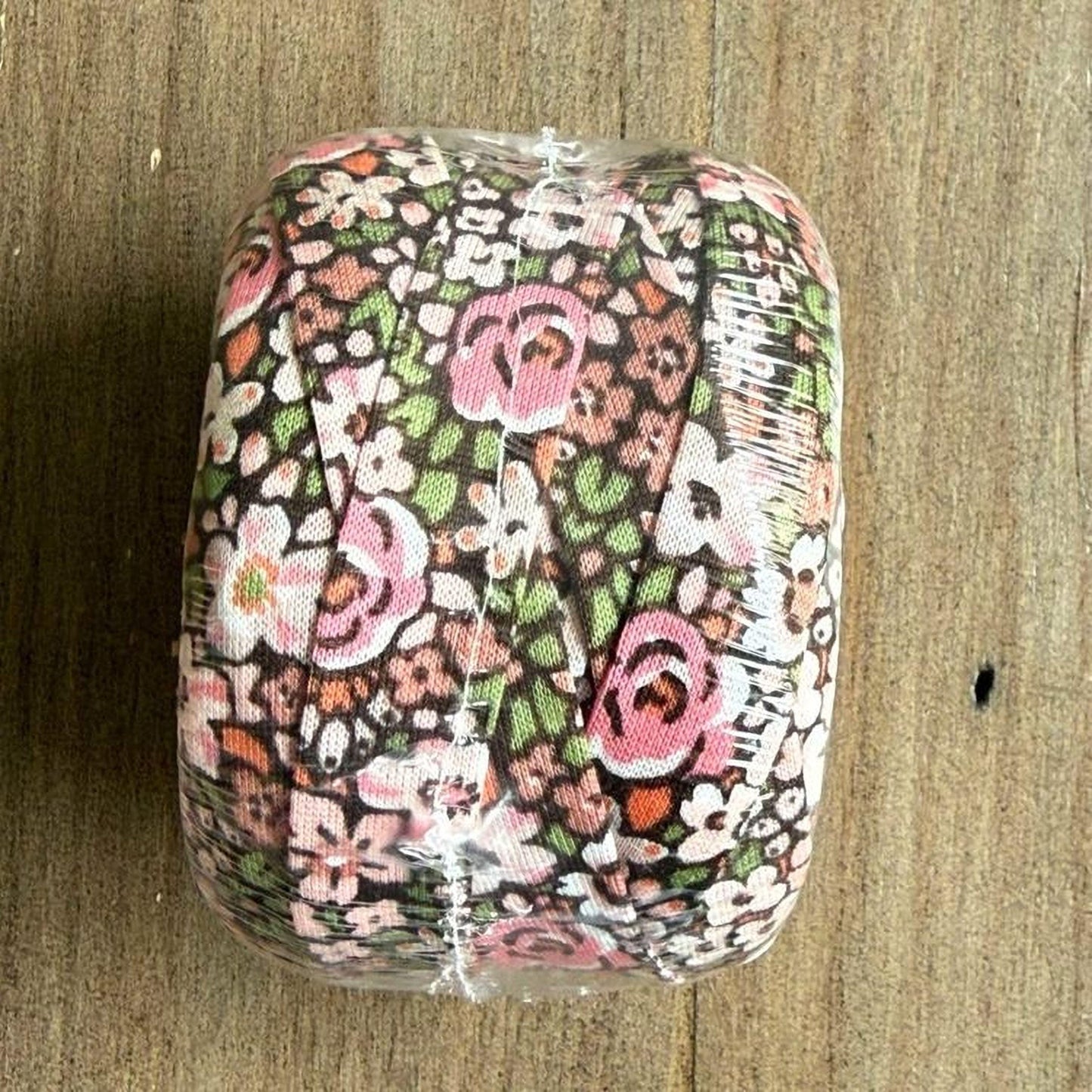 A floral patterned object, possibly a piece of fabric or a decorative item, is wrapped in plastic and placed on a wooden surface.