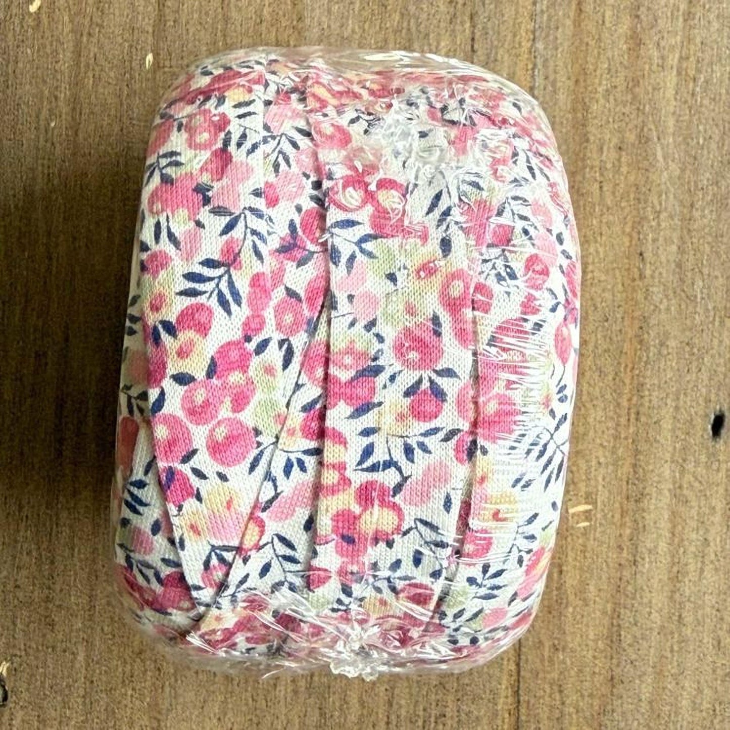 A floral fabric roll is wrapped in clear plastic, placed on a wooden surface.