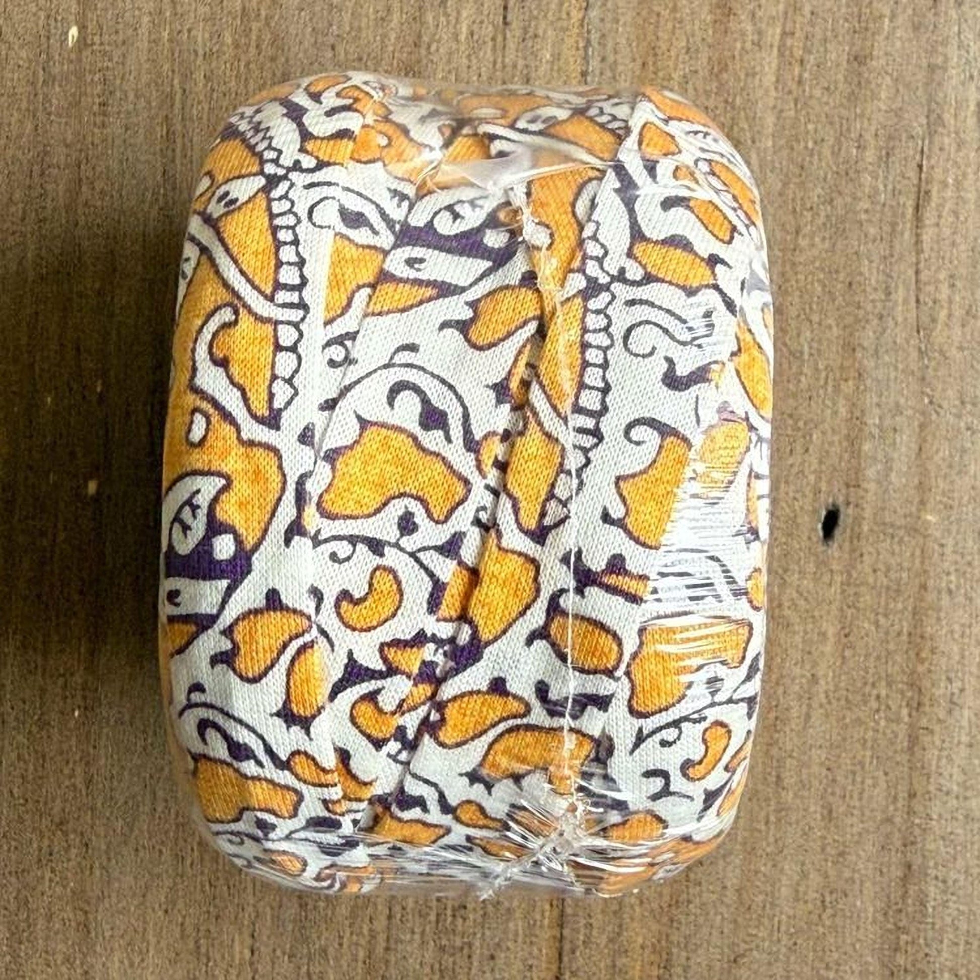 A wrapped object with a patterned fabric covering it, placed on a wooden surface.