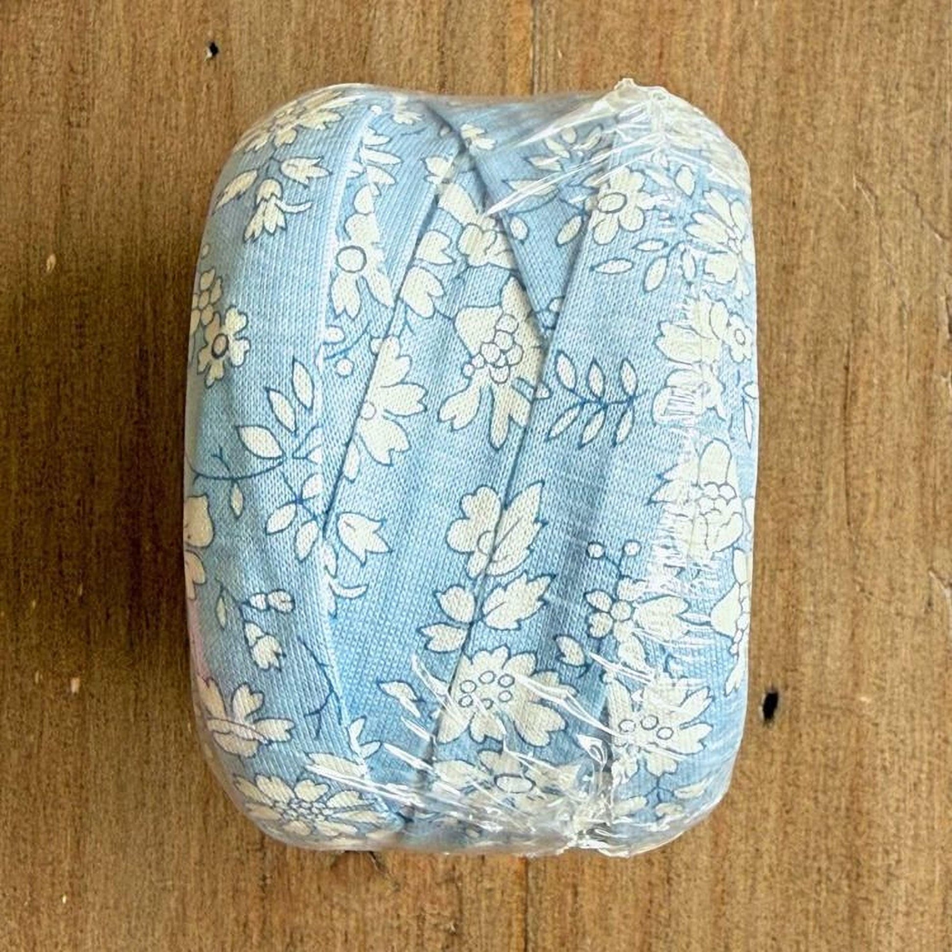 A blue and white floral fabric is wrapped in plastic and placed on a wooden surface.