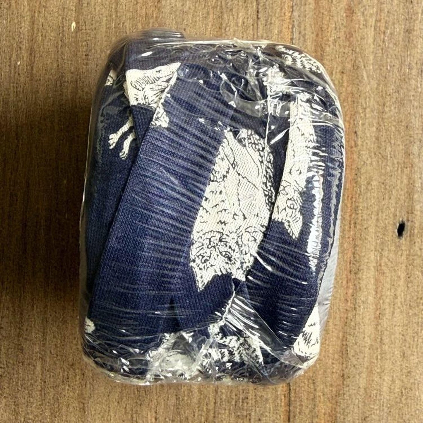 A wrapped object with a patterned fabric, likely a piece of clothing or textile, is placed on a wooden surface.