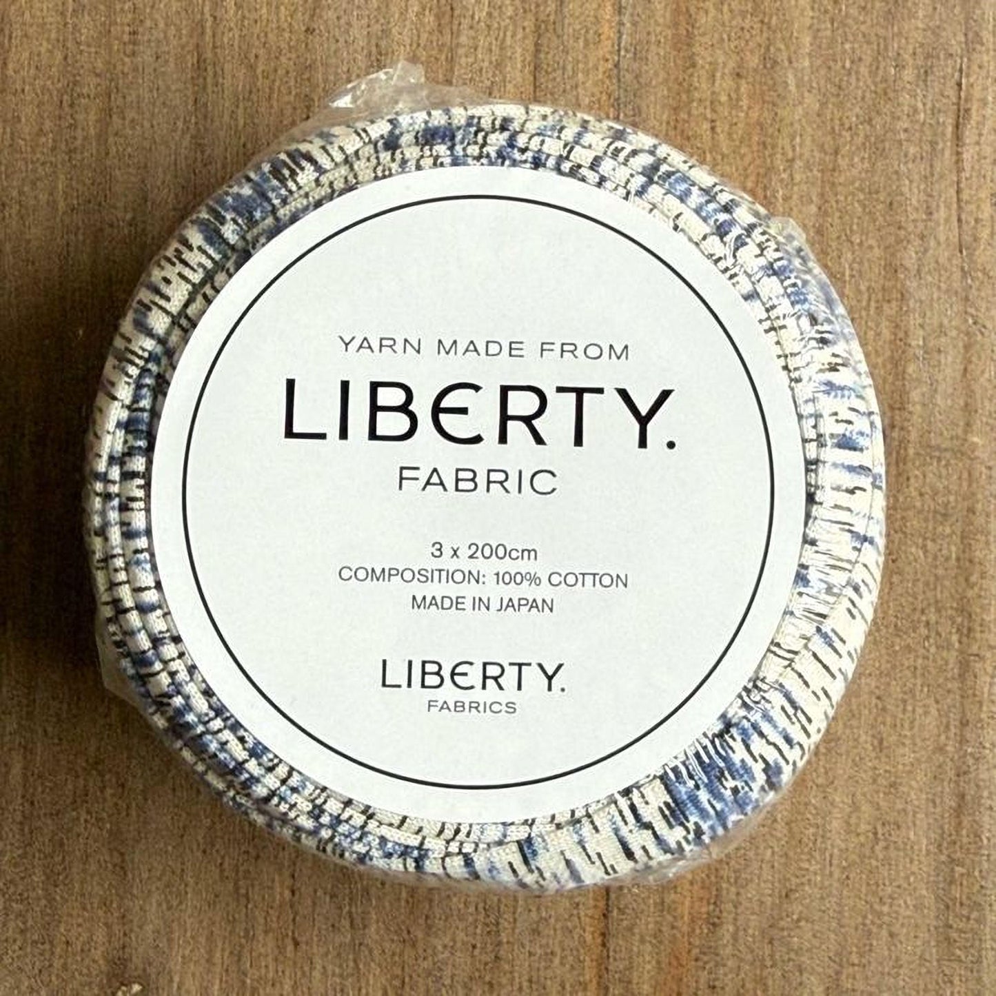 A white label with black text on a circular background, which appears to be a product packaging for a yarn made from Liberty fabric.