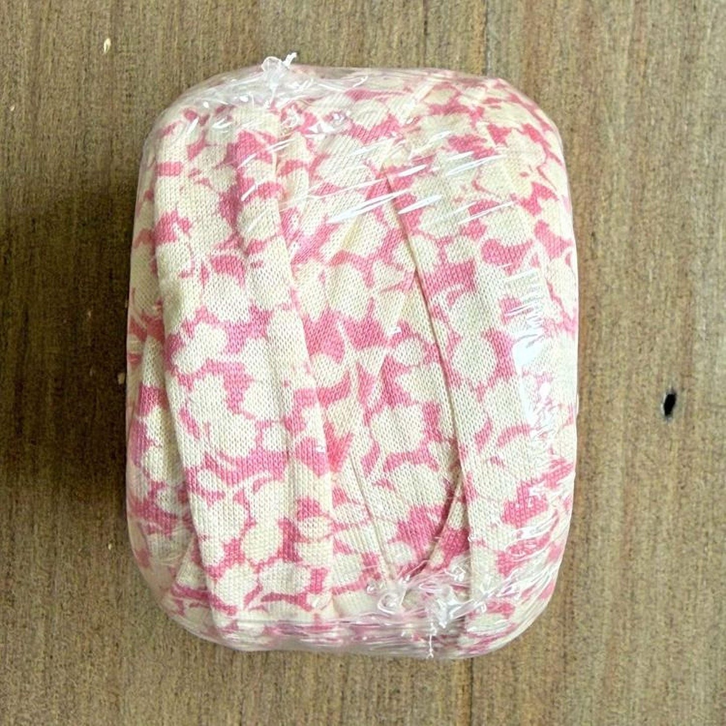 A pink and white floral fabric is wrapped in clear plastic, placed on a wooden surface.