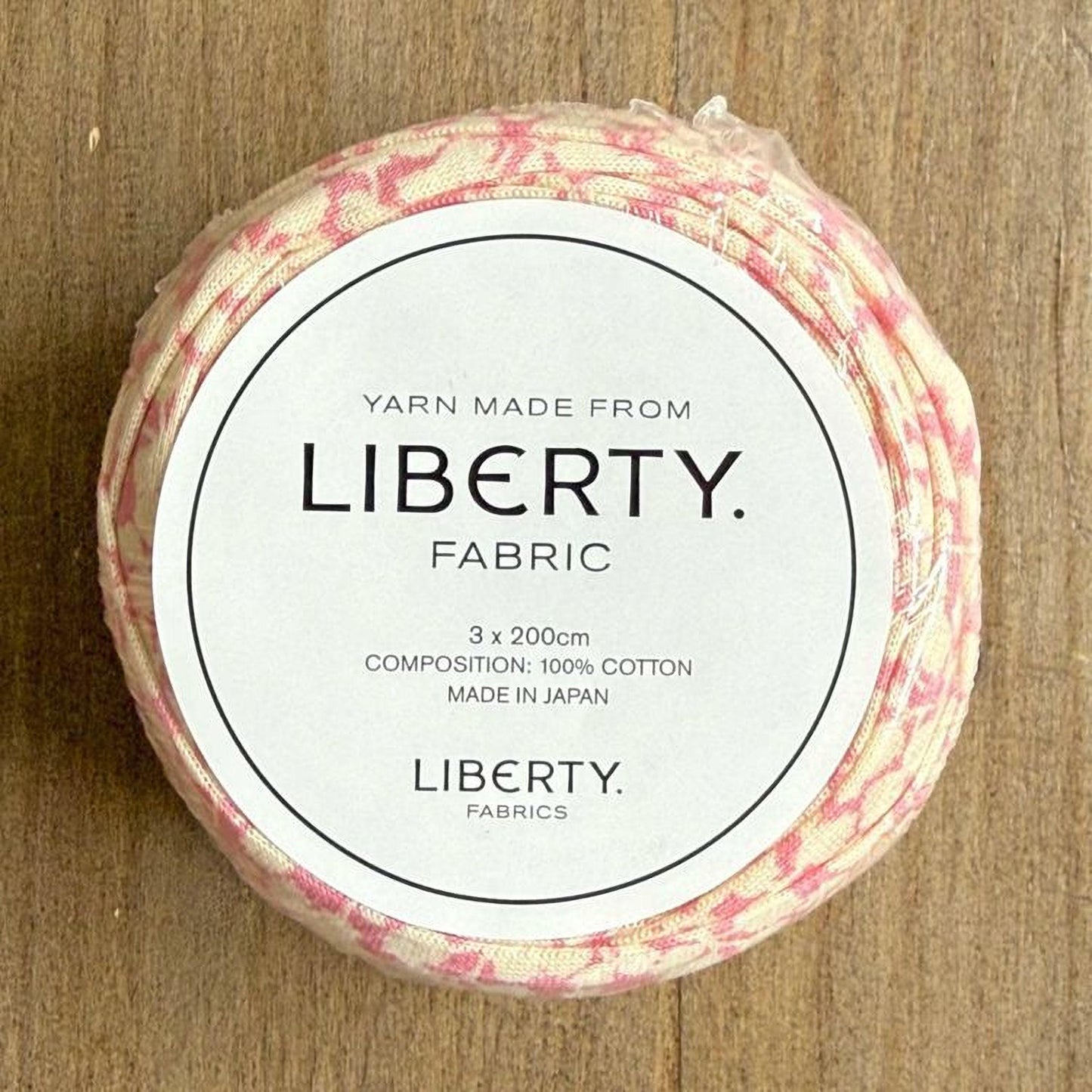 A circular piece of fabric with a label that reads "Yarn Made from LIBERTY. FABRIC 3 x 200cm COMPOSITION: 100% COTTON MADE IN JAPAN LIBERTY. FABRICS".
