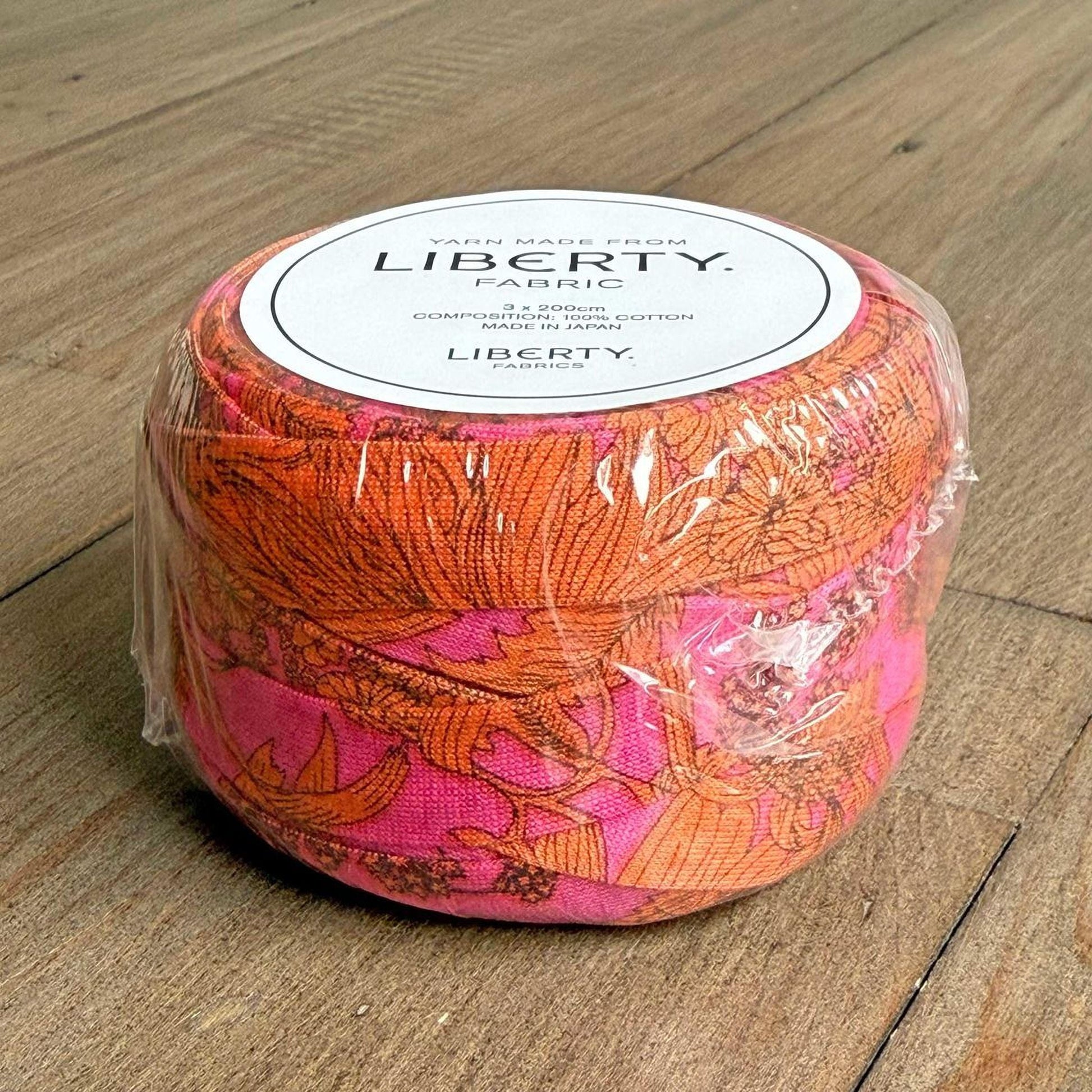 A package of Liberty fabric, which is a type of fabric with a floral pattern, is sitting on a wooden surface.