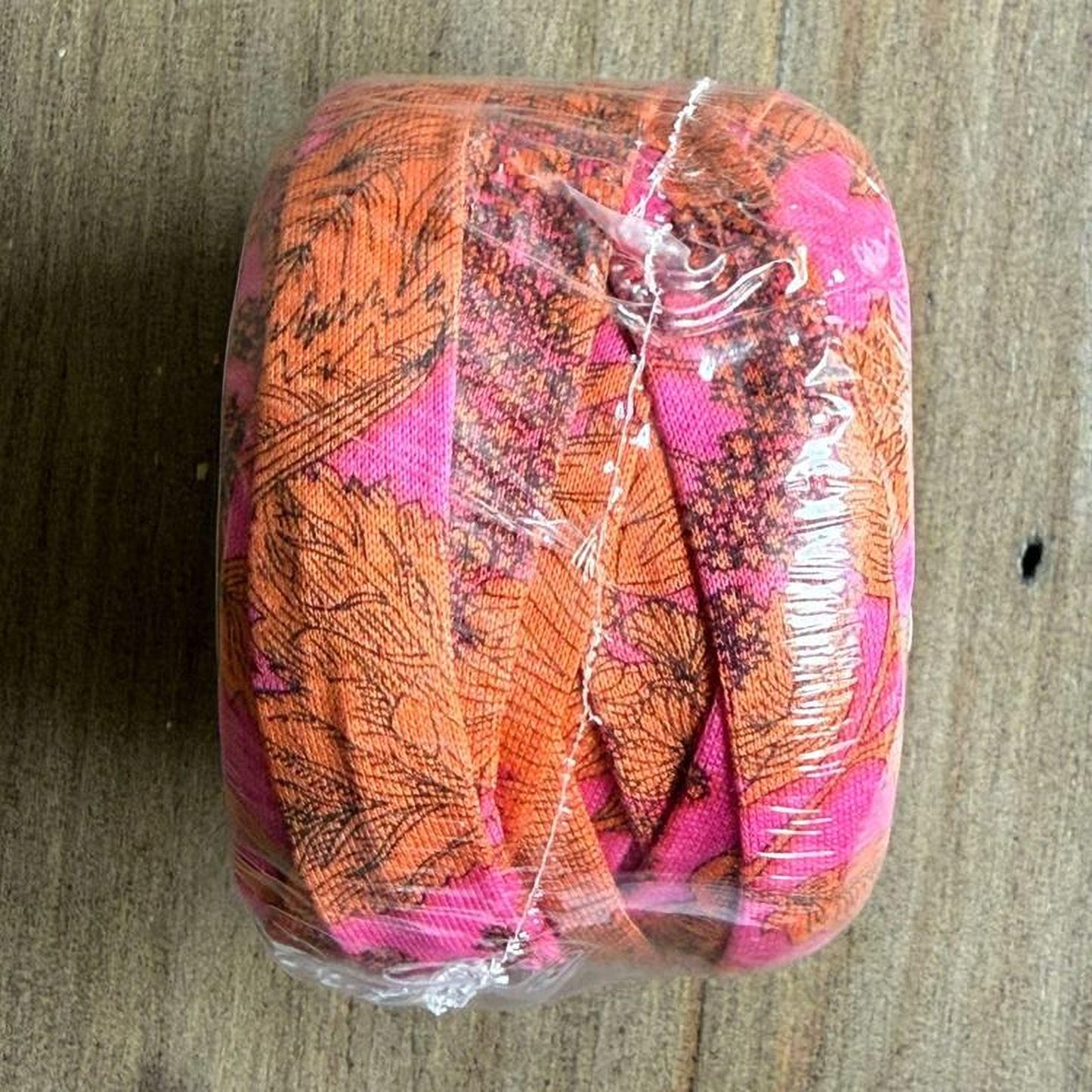 A roll of fabric with a floral pattern in shades of orange and pink, wrapped in plastic and tied with a string.