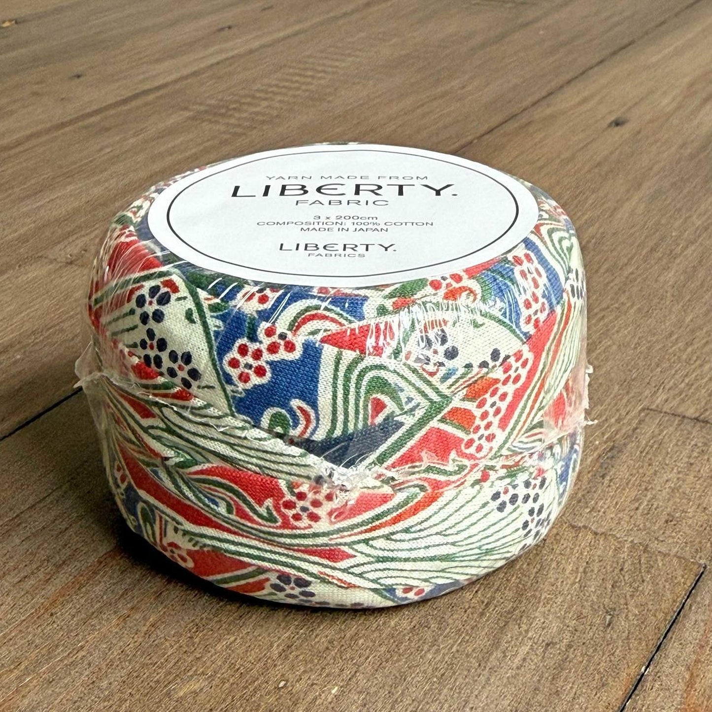 A package of Liberty fabric, featuring a colorful, patterned design, sits on a wooden surface.