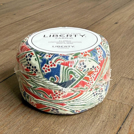 A package of Liberty fabric, featuring a colorful, patterned design, sits on a wooden surface.