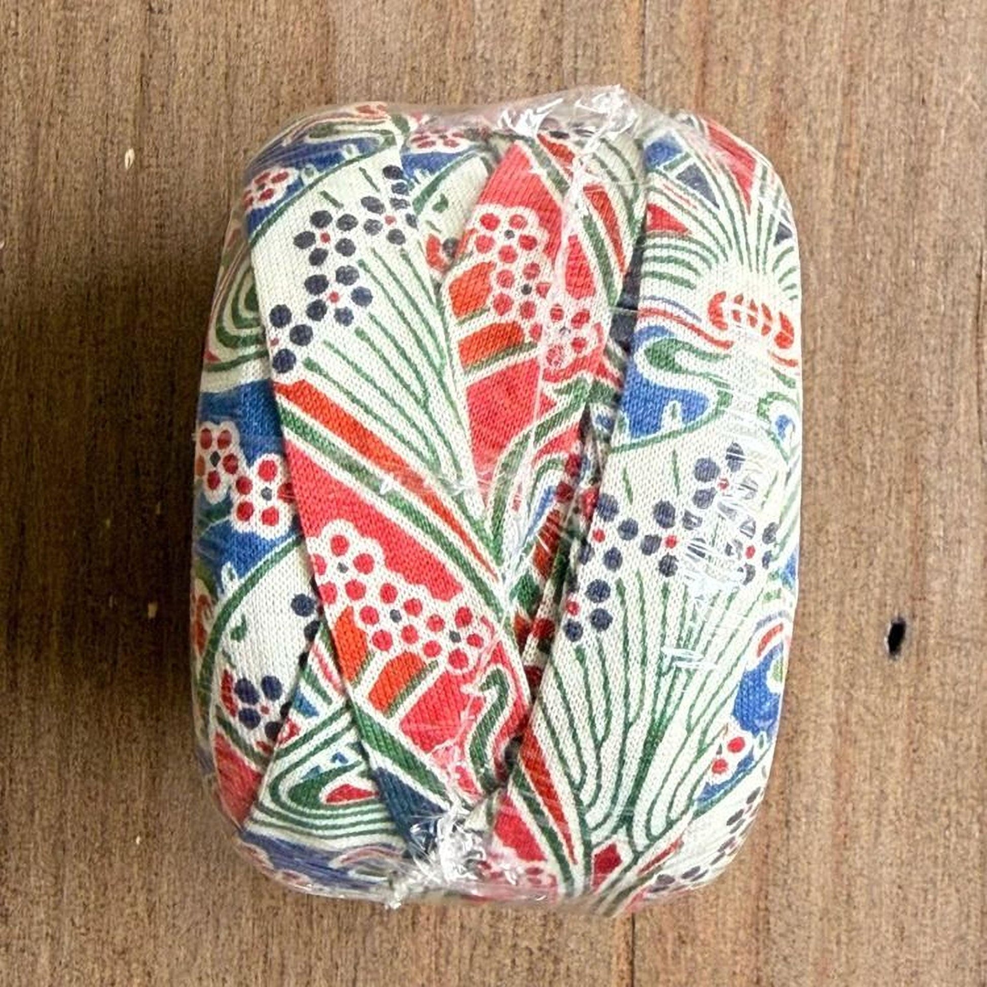 A colorful, patterned object wrapped in plastic, sitting on a wooden surface.