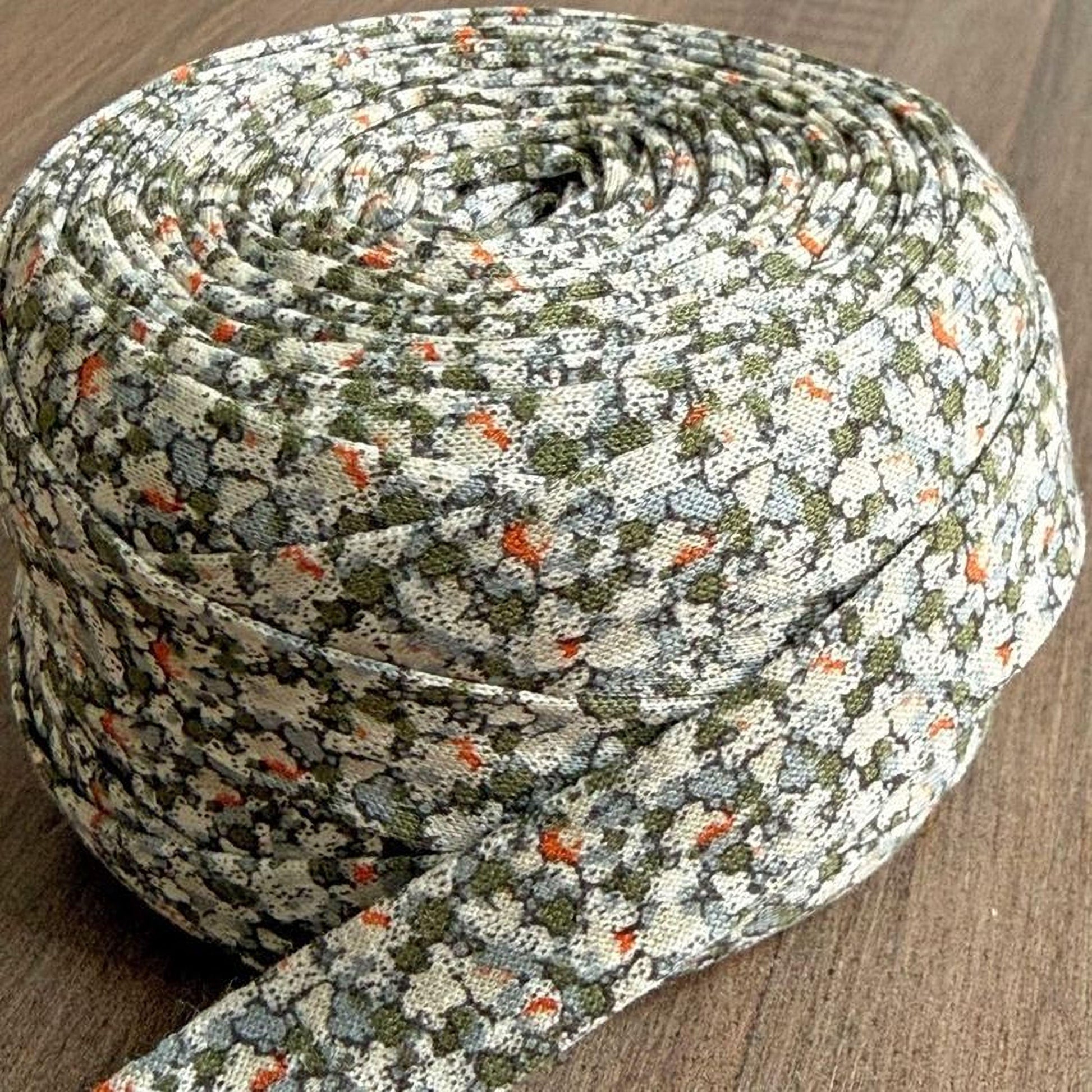 A close-up image of a spool of fabric with a floral pattern, resting on a wooden surface.