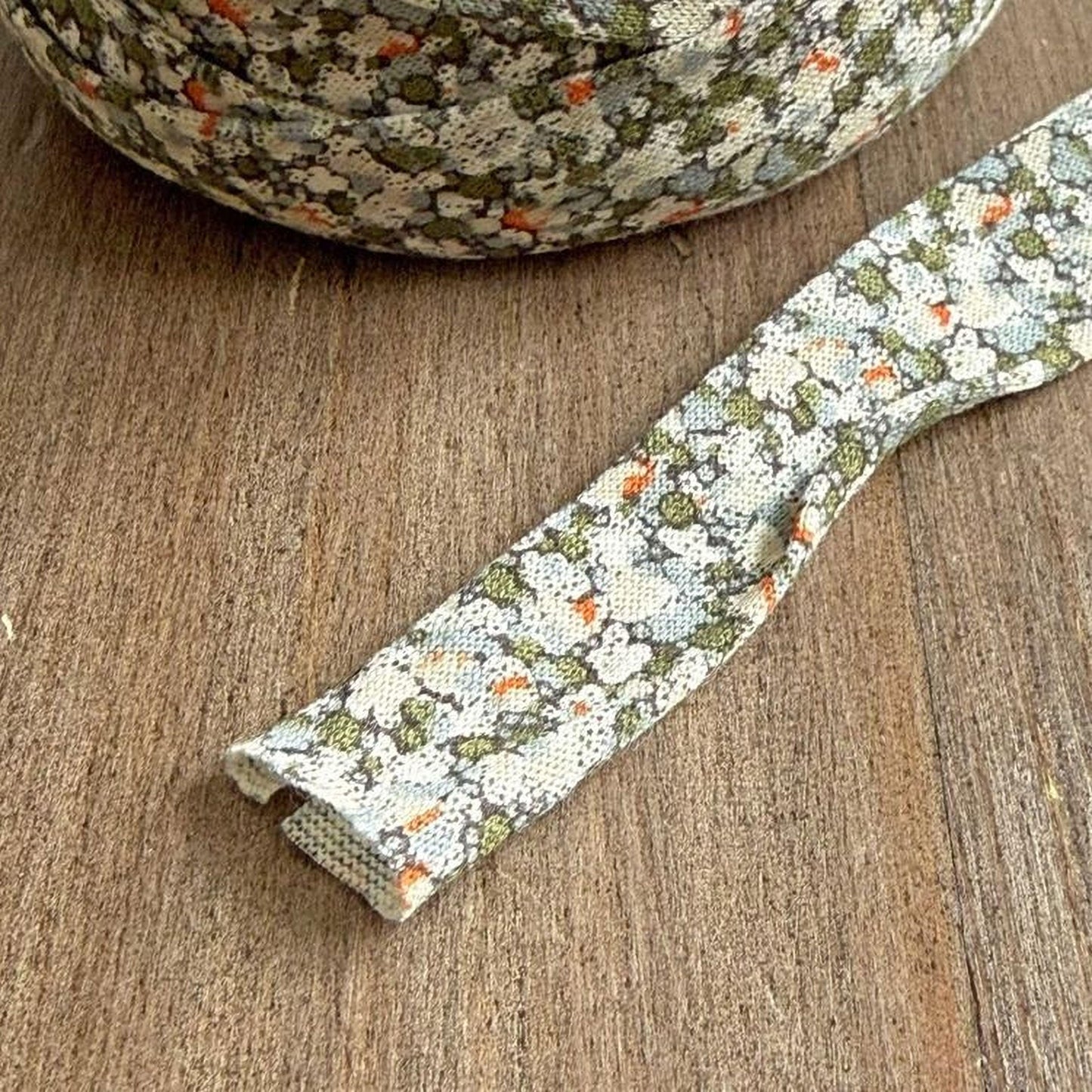A spool of multicolored fabric with a floral pattern is lying on a wooden surface.