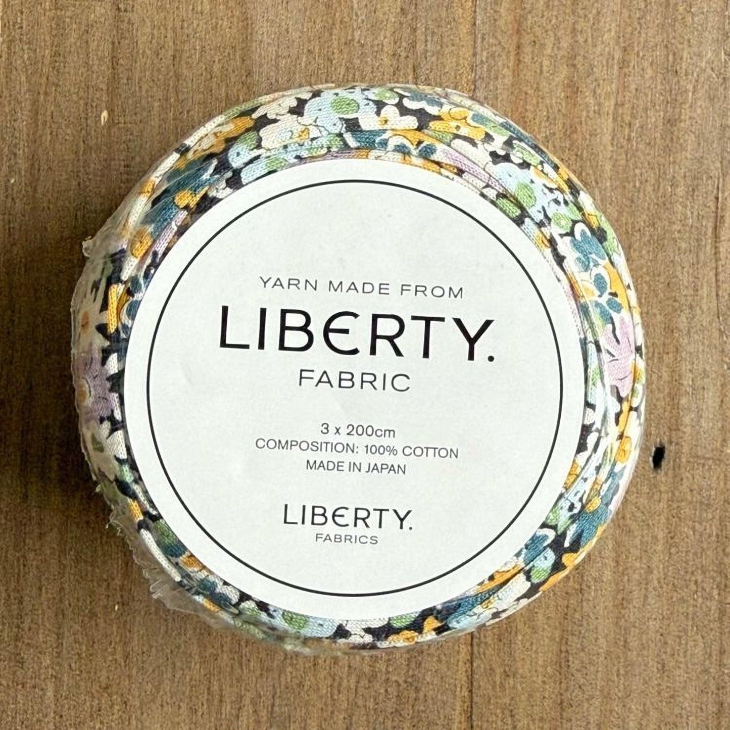 A spool of yarn with a label that reads "Yarn Made from LIBERTY. FABRIC" and provides details about the product, including its composition and origin.