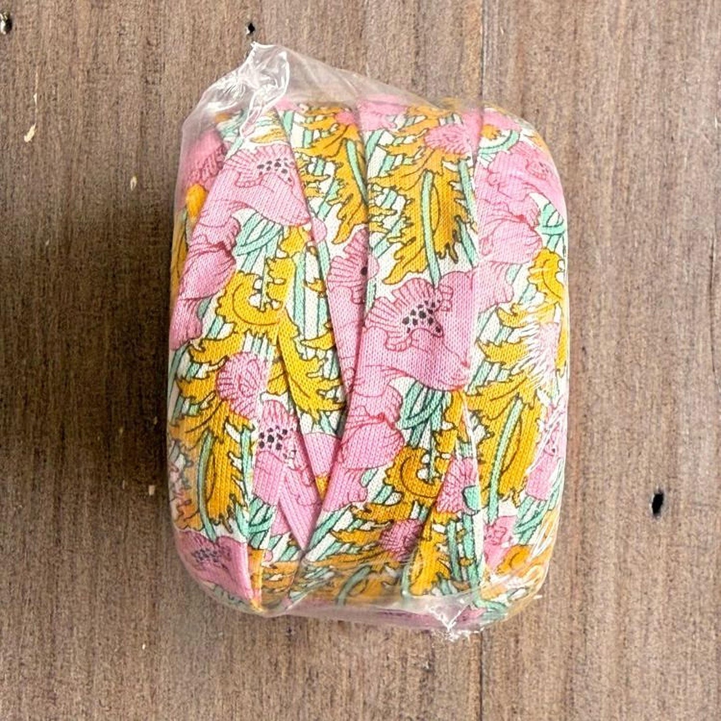 A clear plastic bag containing a colorful floral patterned fabric, placed on a wooden surface.