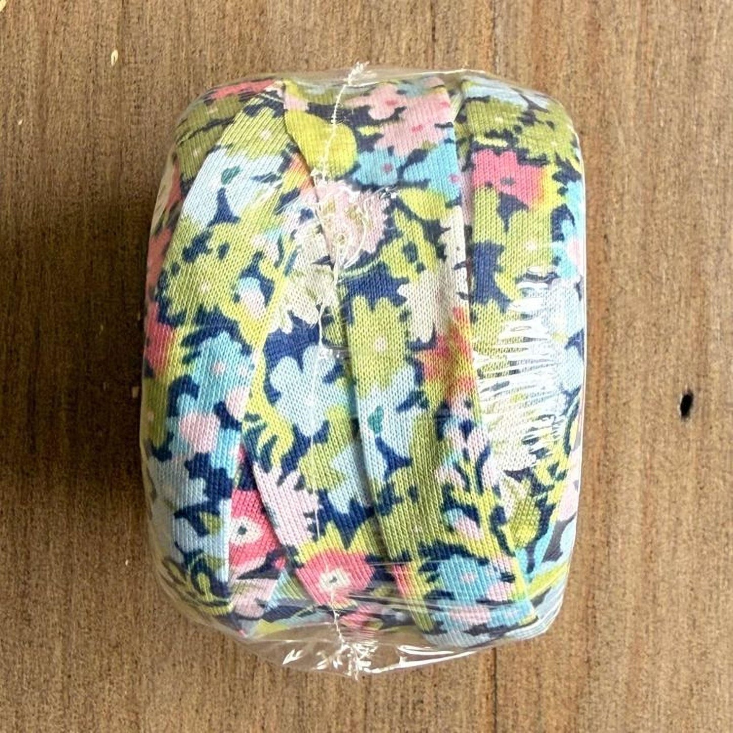 A roll of colorful floral fabric is wrapped in plastic and placed on a wooden surface.