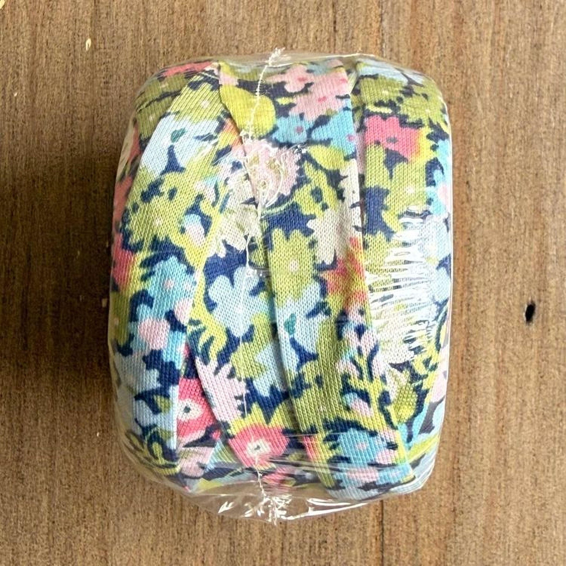 A roll of colorful floral fabric is wrapped in plastic and placed on a wooden surface.