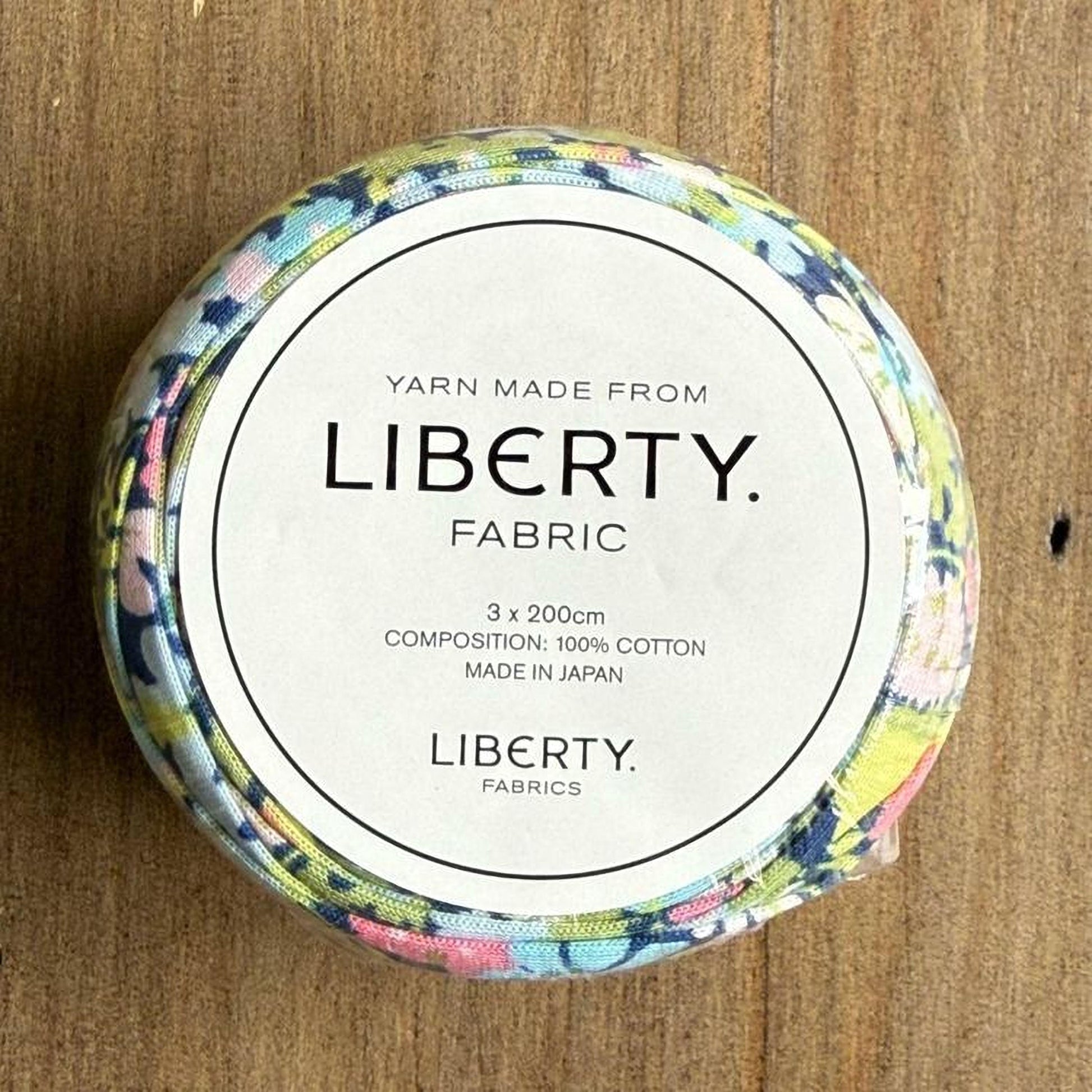 A round spool of yarn with a floral pattern, labeled as "Yarn Made from Liberty. Fabric".