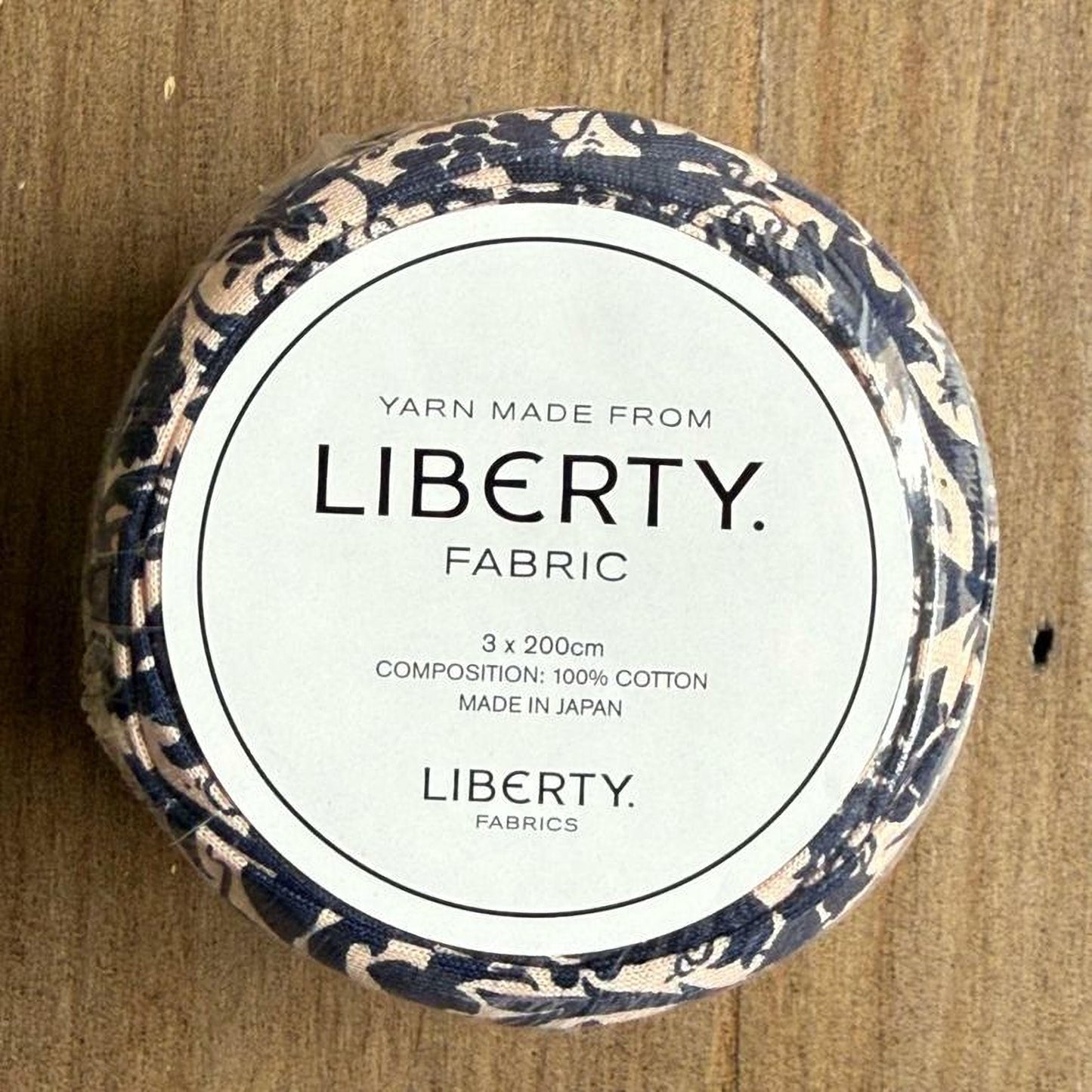 A round container with a label that reads "Yarn Made from LIBERTY. FABRIC" and provides details about the product, including its composition and manufacturing origin.