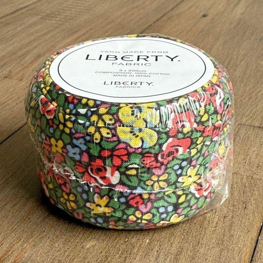 A package of Liberty fabric, featuring a colorful floral pattern, is sitting on a wooden surface.
