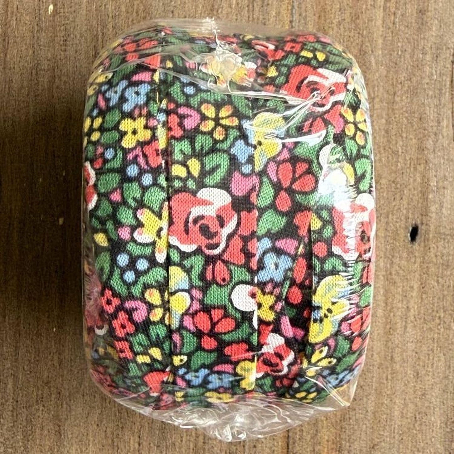 A colorful floral patterned object, possibly a piece of fabric or a decorative item, is wrapped in clear plastic and placed on a wooden surface.