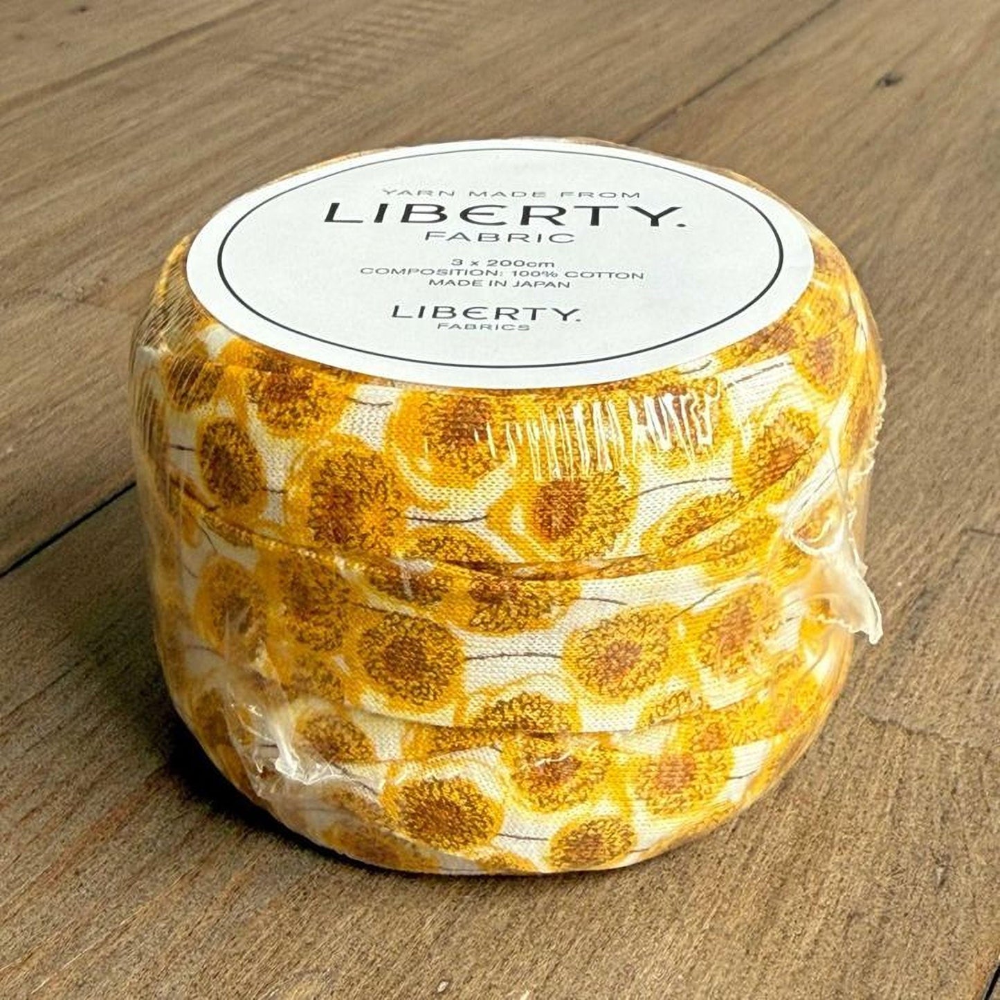 A round container with a white label that reads "Yarn made from LIBERTY Fabric" and "Made in Japan". The container has a yellow and white pattern resembling sunflowers or flowers.