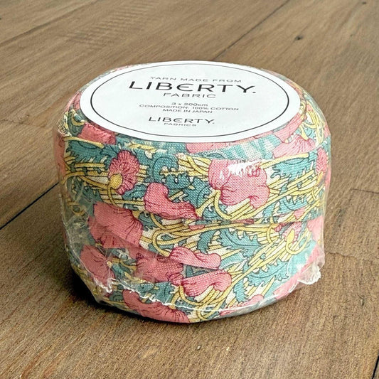 A package of Liberty fabric, featuring a colorful floral pattern, is sitting on a wooden surface.