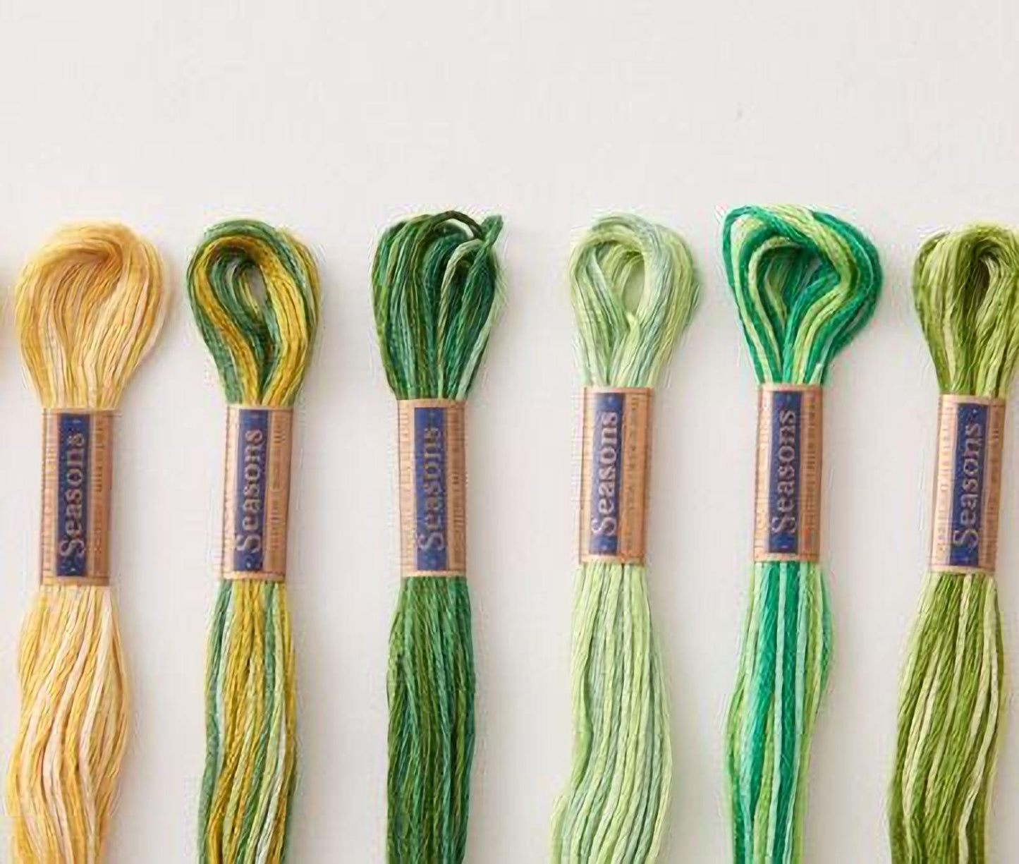A collection of six spools of thread in various colors, including yellow, green, and blue, arranged on a white background.