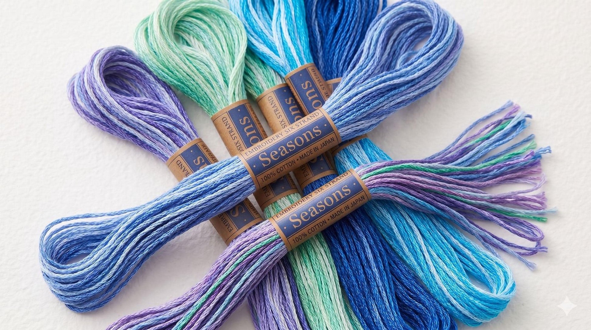 A collection of colorful thread spools with blue, green, and purple hues, arranged on a white background.