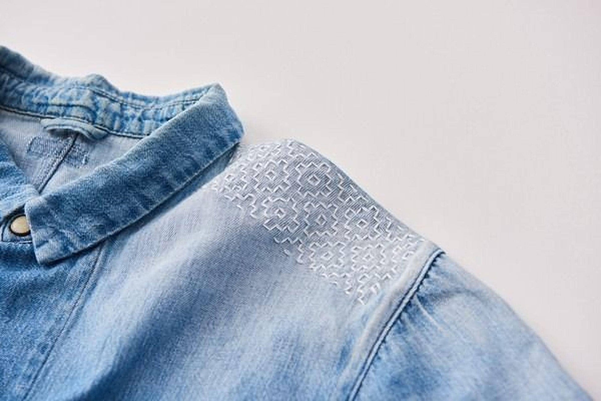A close-up view of a denim shirt with a white embroidered patch on the shoulder.