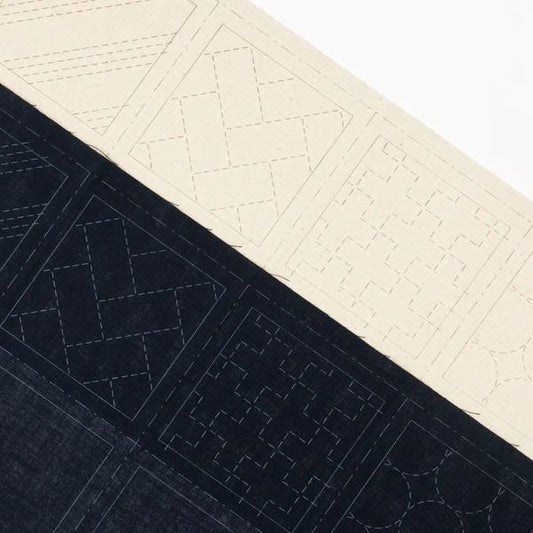 a close-up view of a fabric with a geometric pattern, including a diamond shape and a square shape. The fabric appears to be a dark-colored material, possibly denim or a similar type of fabric.