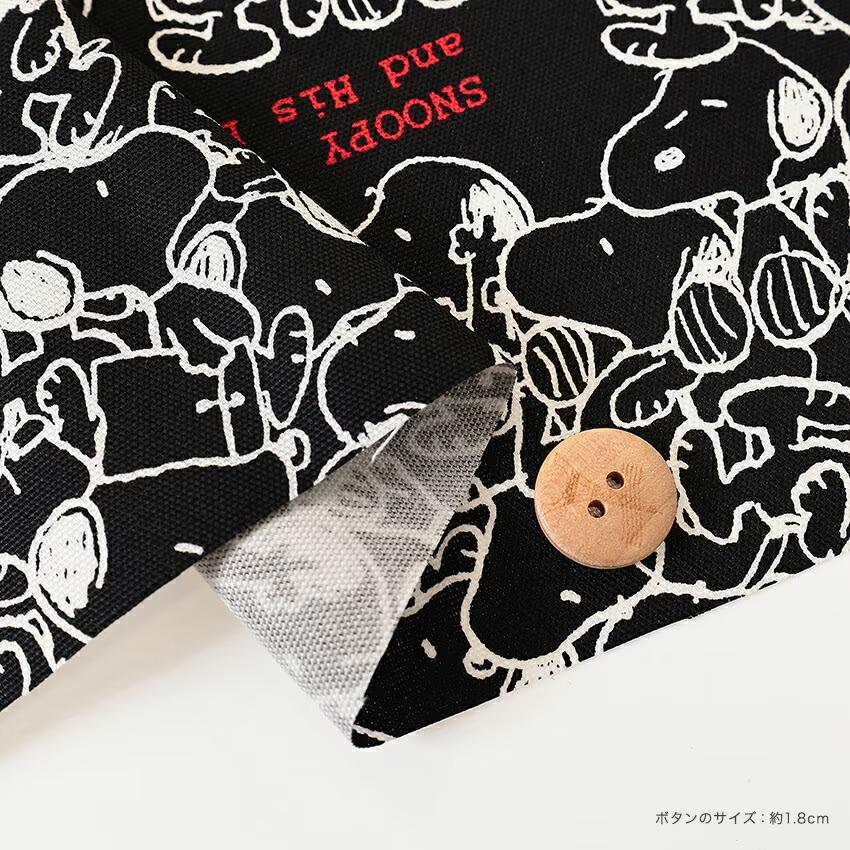 a close-up view of a black and white fabric with a playful, cartoon-like design of a character resembling a dog. The fabric appears to be a piece of clothing or textile, with a wooden button visible on the right side.