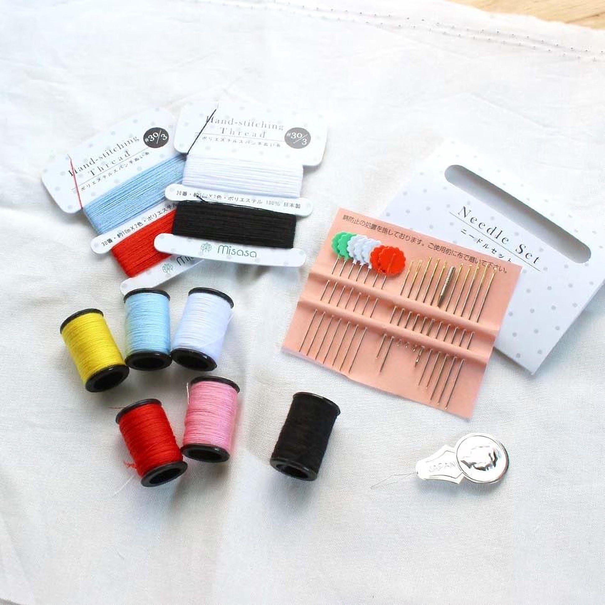 various sewing and crafting supplies, including spools of thread in different colors, needles, a needle set, and a pin cushion.