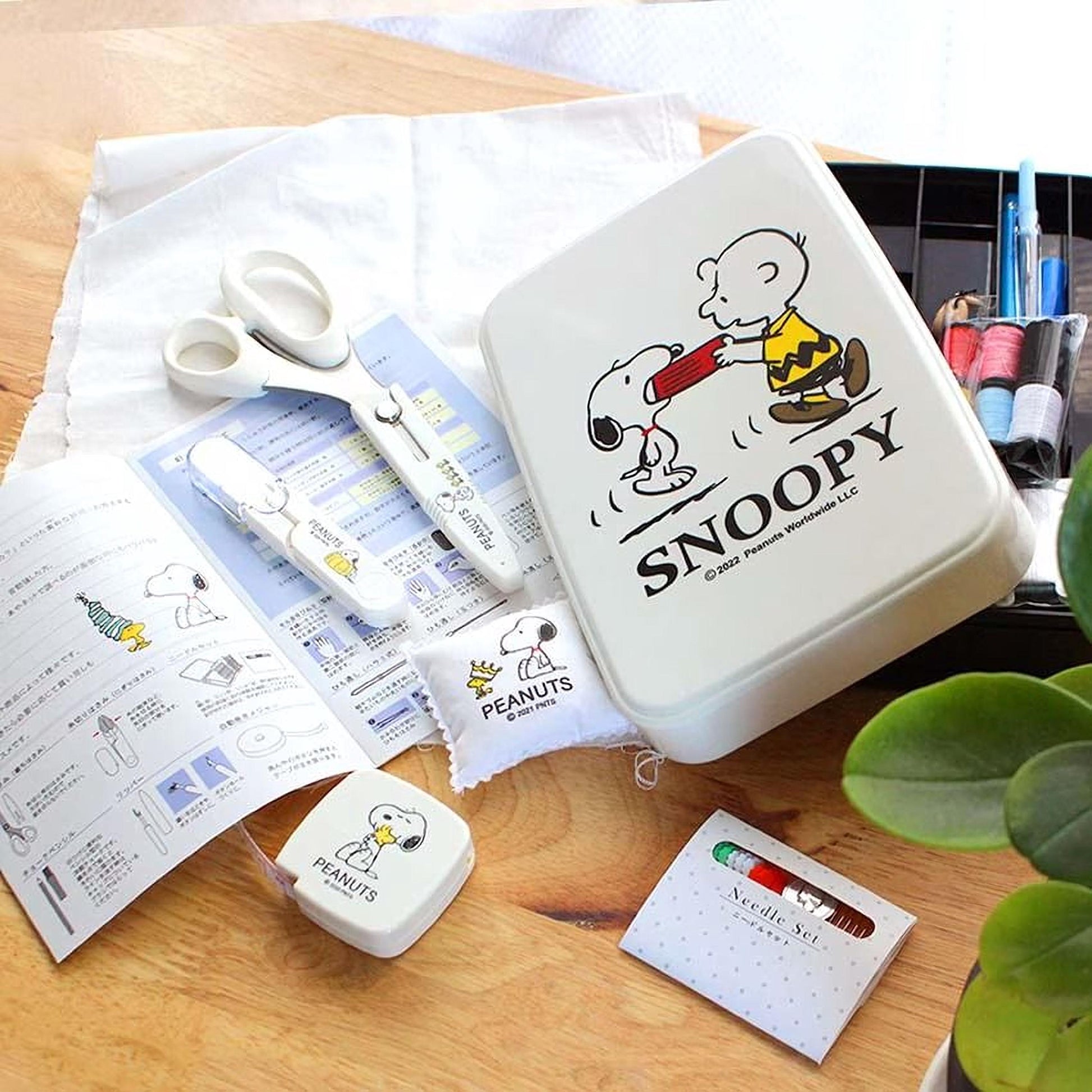 A collection of Peanuts-themed items, including a sewing kit, scissors, and a sewing pattern, arranged on a wooden surface.