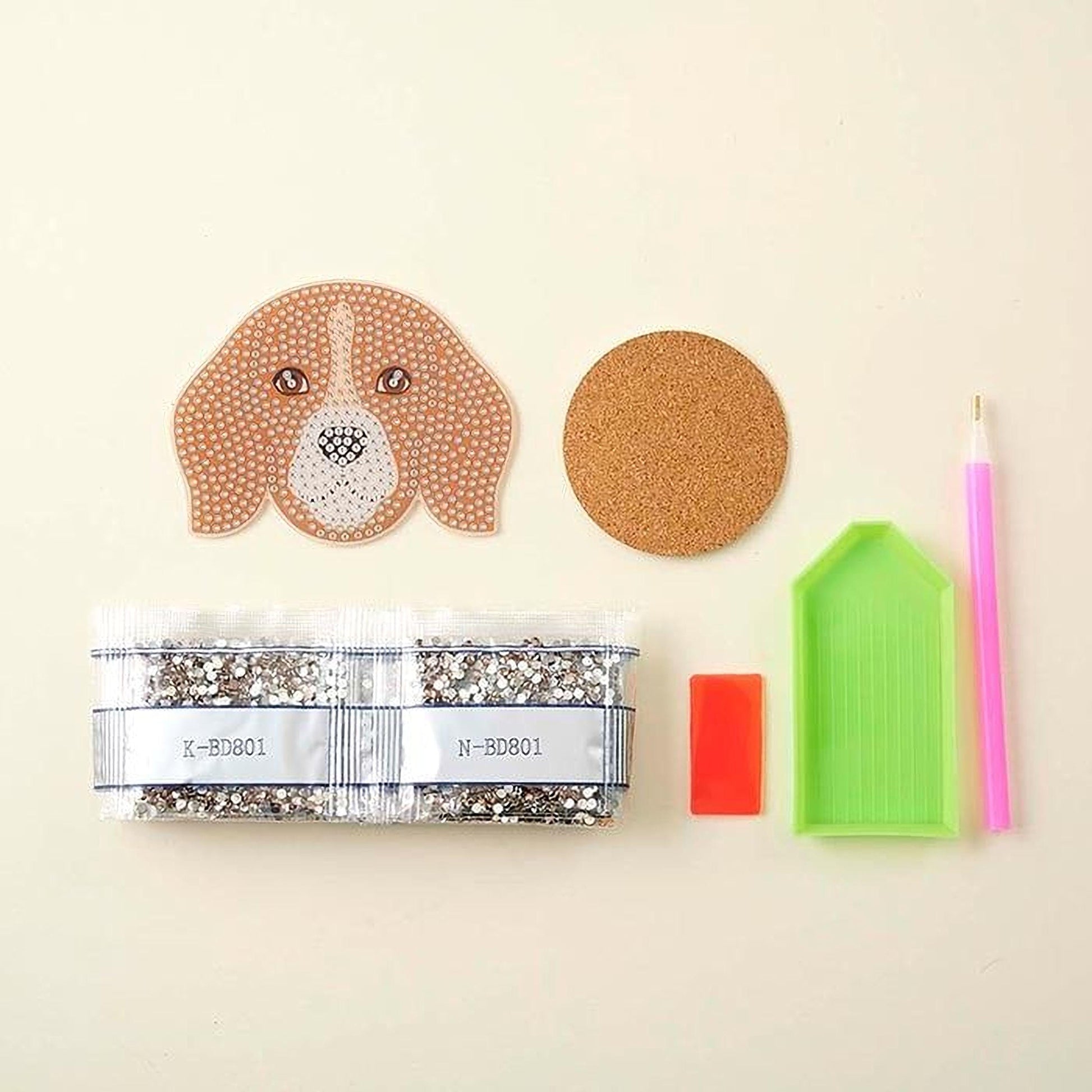various craft supplies, including a dog-shaped rhinestone, a cork coaster, a pen, a package of rhinestone beads, and a diamond tool.