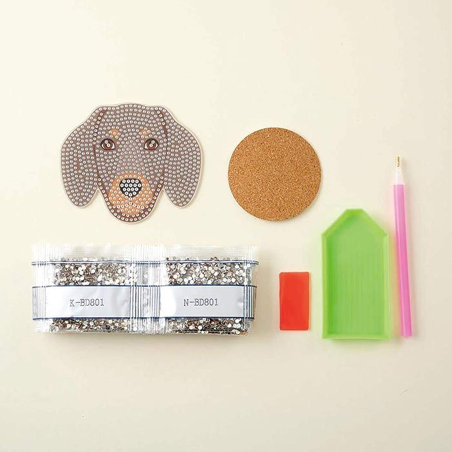 various craft supplies, including a package of rhinestones, a cork coaster, a pen, and a diamond-patterned object.