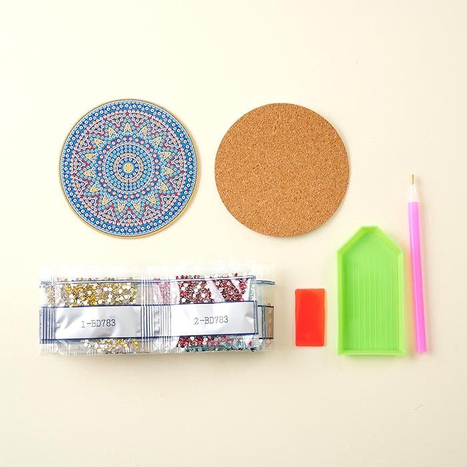 various craft supplies, including a blue and white patterned coaster, a cork coaster, a clear plastic tray, a pink and white pen, and a red and white patterned bag.