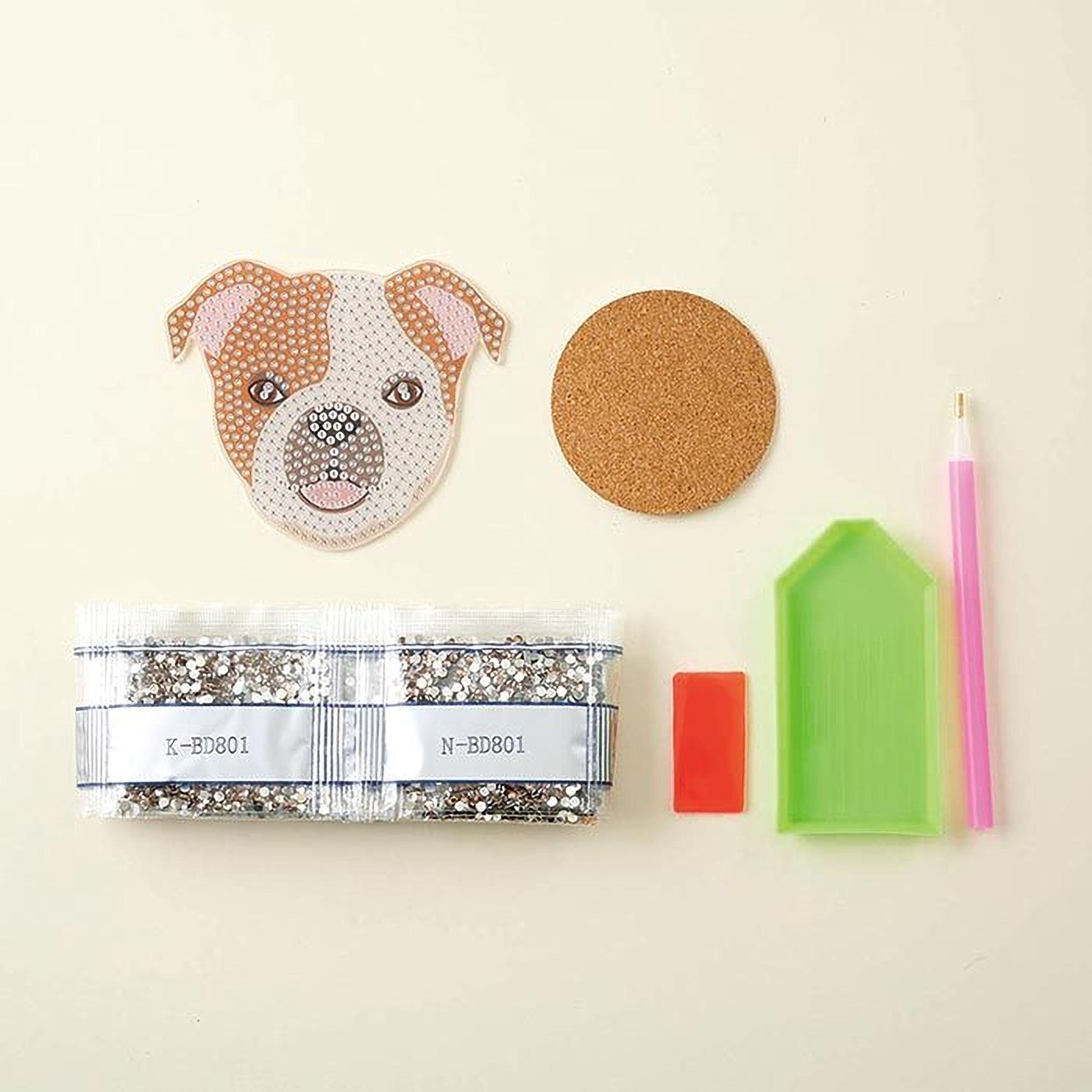 various craft supplies, including a dog-shaped paper, a cork coaster, a pen, a small bag of glitter, and a diamond tool.