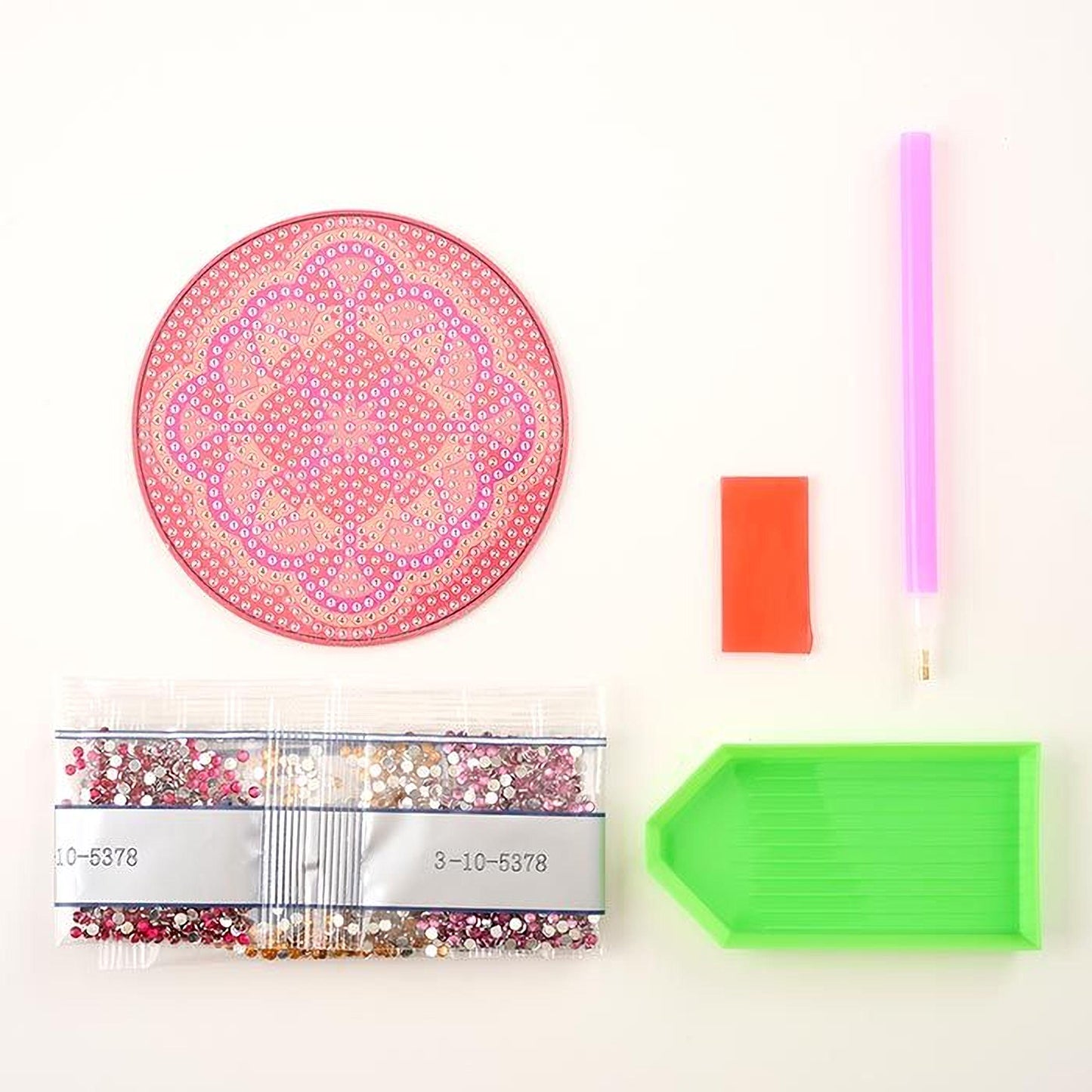 various craft supplies, including a pink and white patterned mat, a green and orange rectangular tray, a pink and purple pen, a red and orange rectangular object, and a clear plastic bag filled with small, colorful beads.