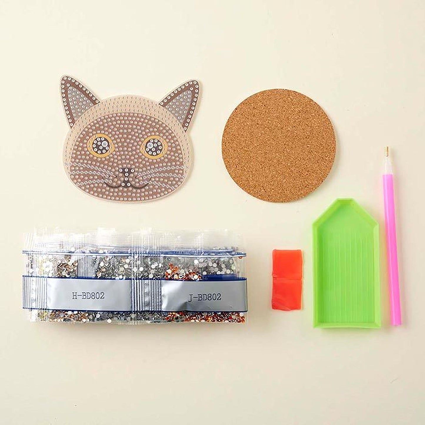various craft supplies, including a cat-shaped object, a cork coaster, a pen, a bag of rhinestones, and a diamond-shaped object.